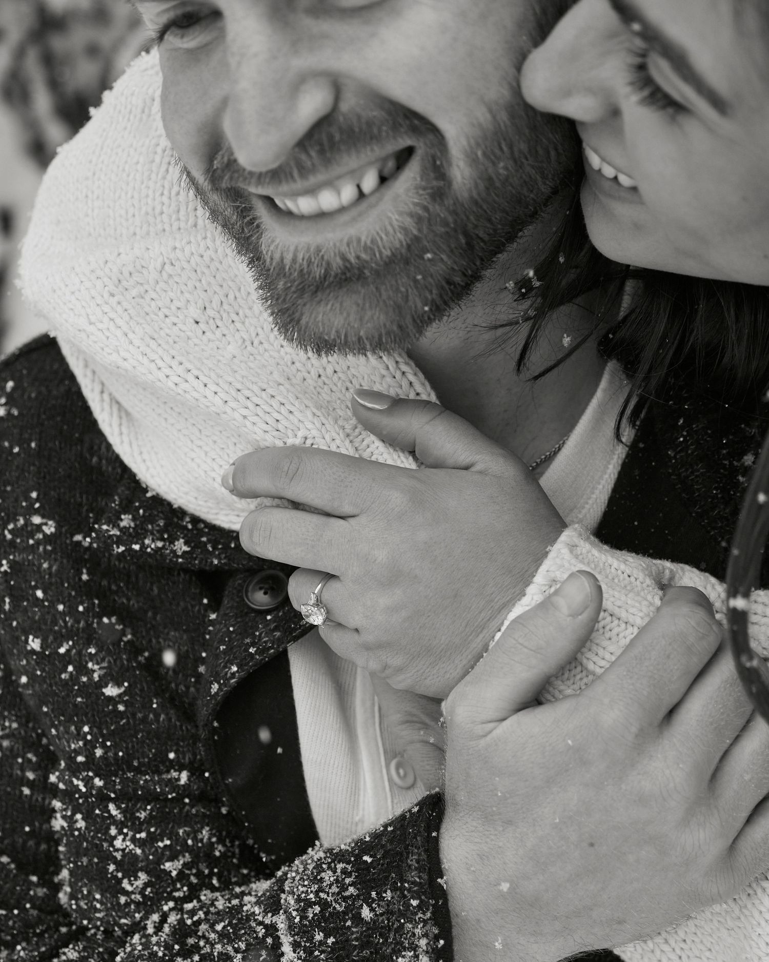 A tender embrace captured in black and white with snow falling around a cozy winter scene.