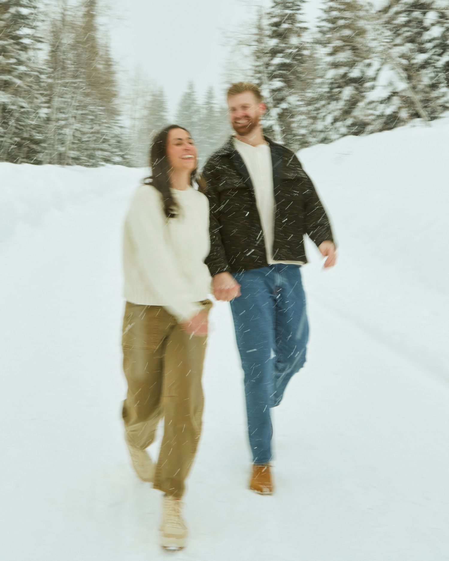 Candid winter scene of two people walking through falling snow in warm clothing.