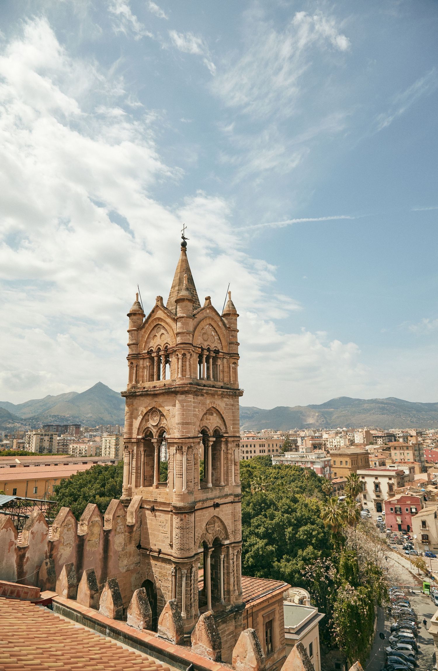 Gothic church tower rising above Palermo cityscape with mountains in background.