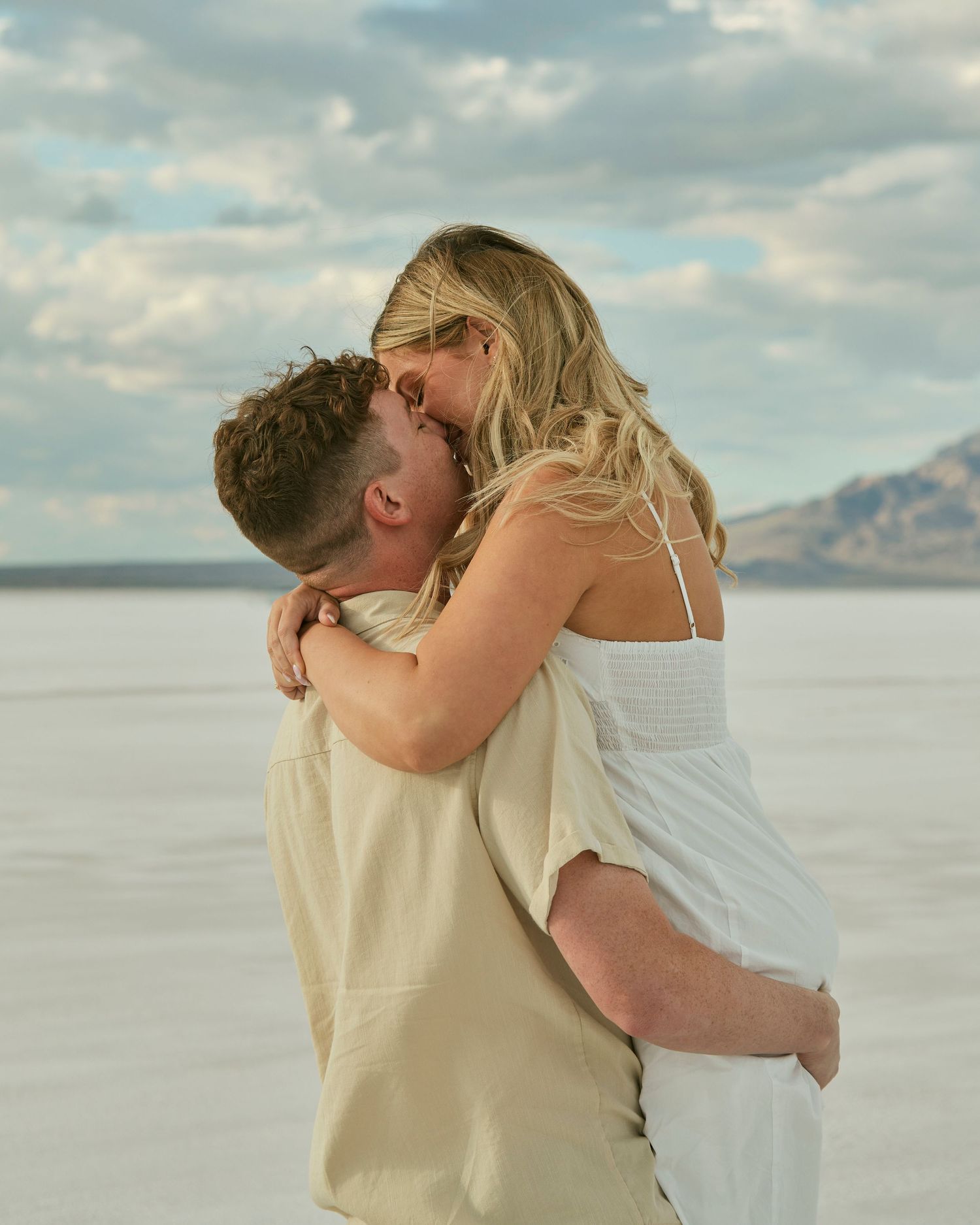 A joyful embrace between newly engaged couple on salt flats with mountains in background.