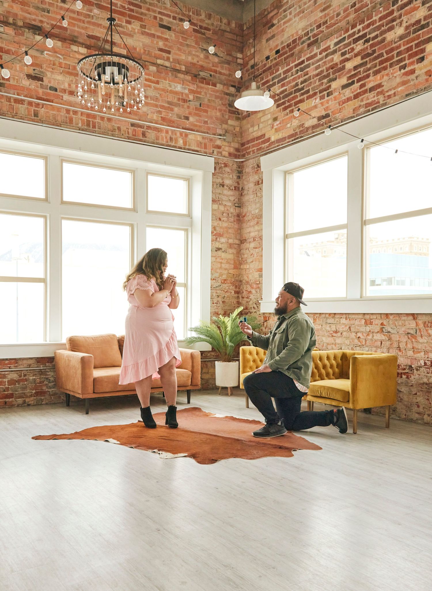 A proposal scene in a bright room with exposed brick walls and modern furniture.