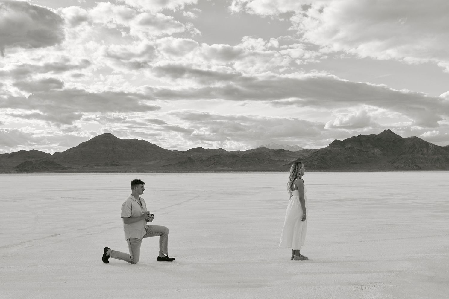 Black and white proposal photograph on salt flats with dramatic mountain backdrop.
