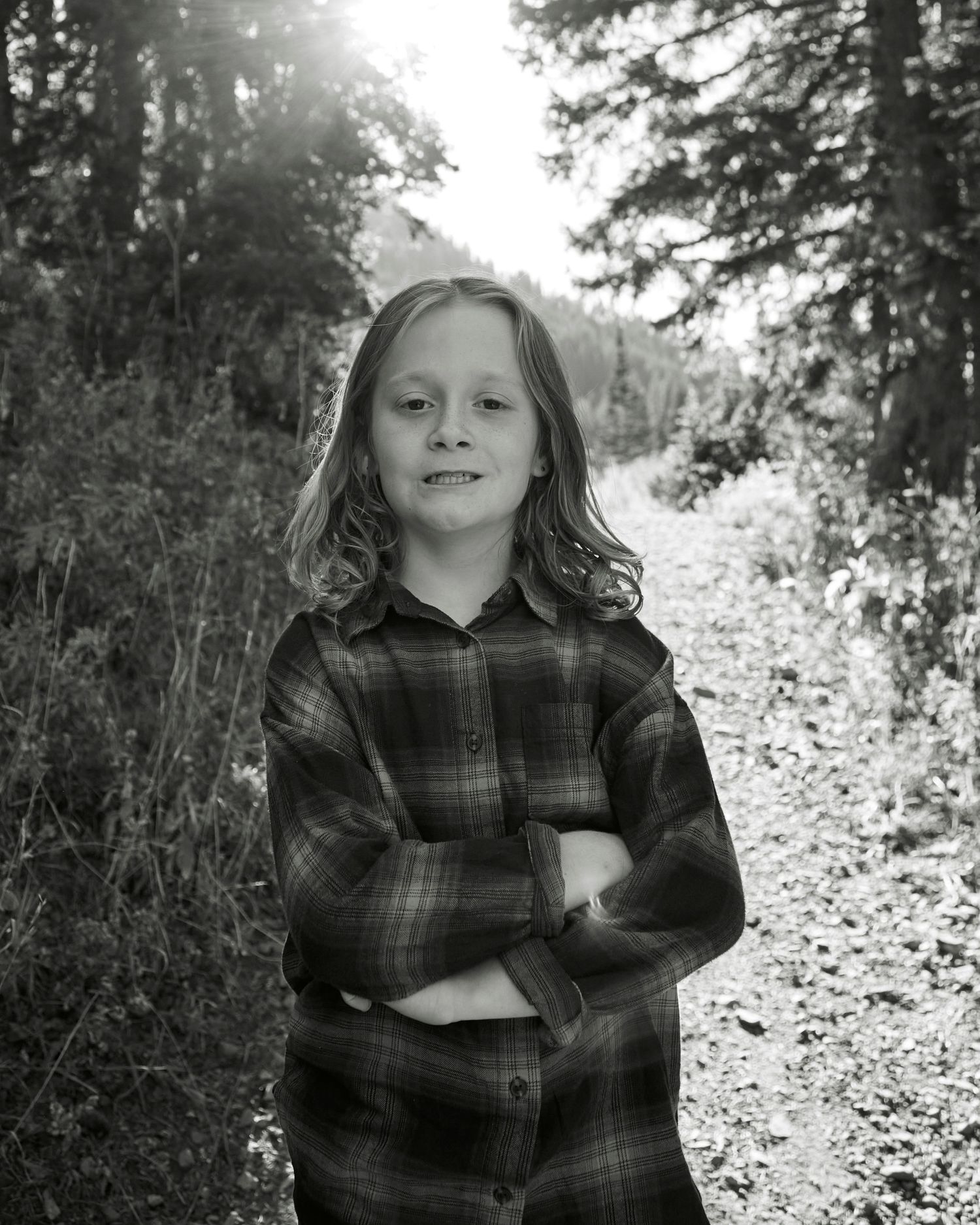 Black and white portrait of a child in plaid hoodie standing confidently on a forest path.