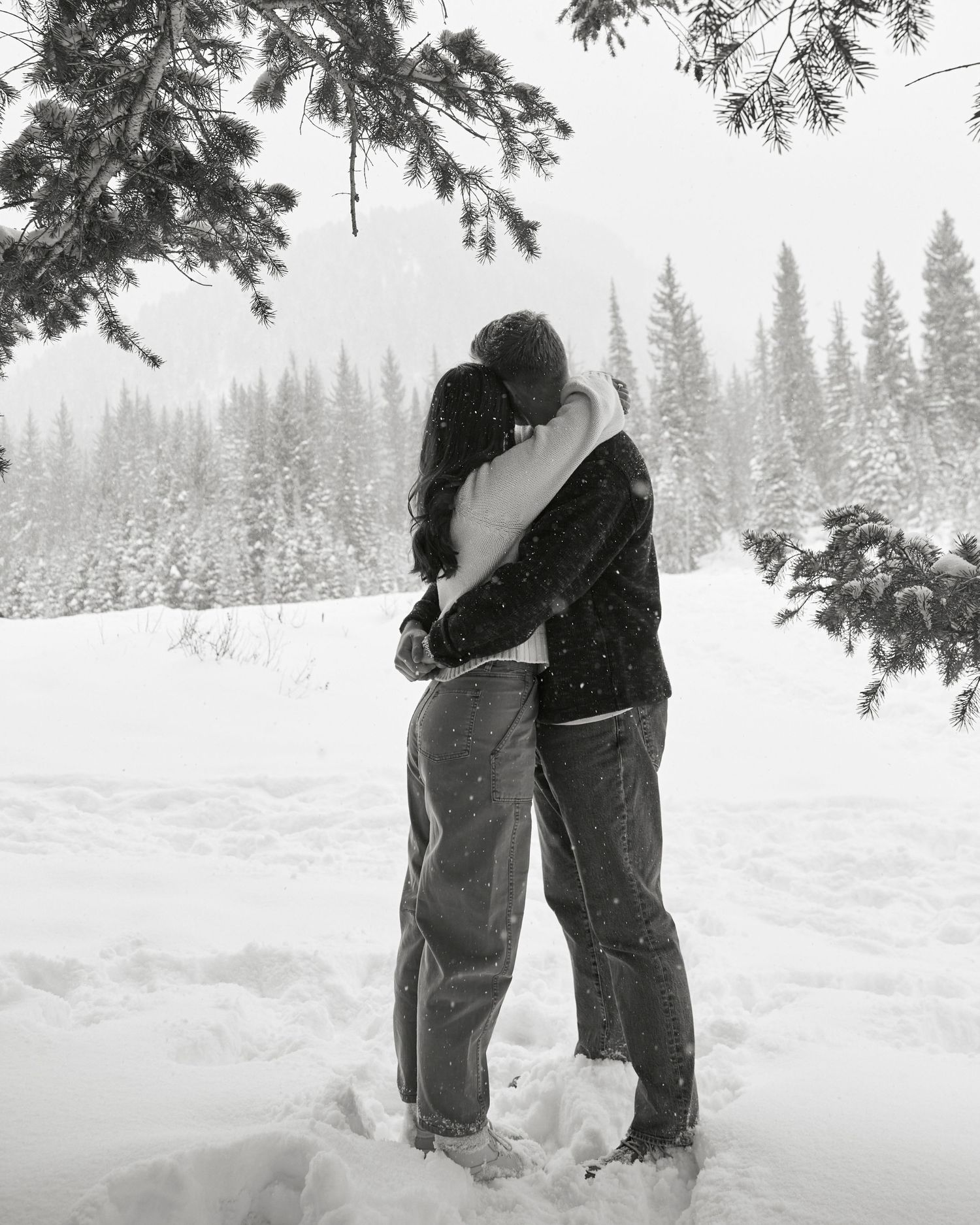 Romantic embrace between couple in snowy forest with evergreen trees in winter landscape.
