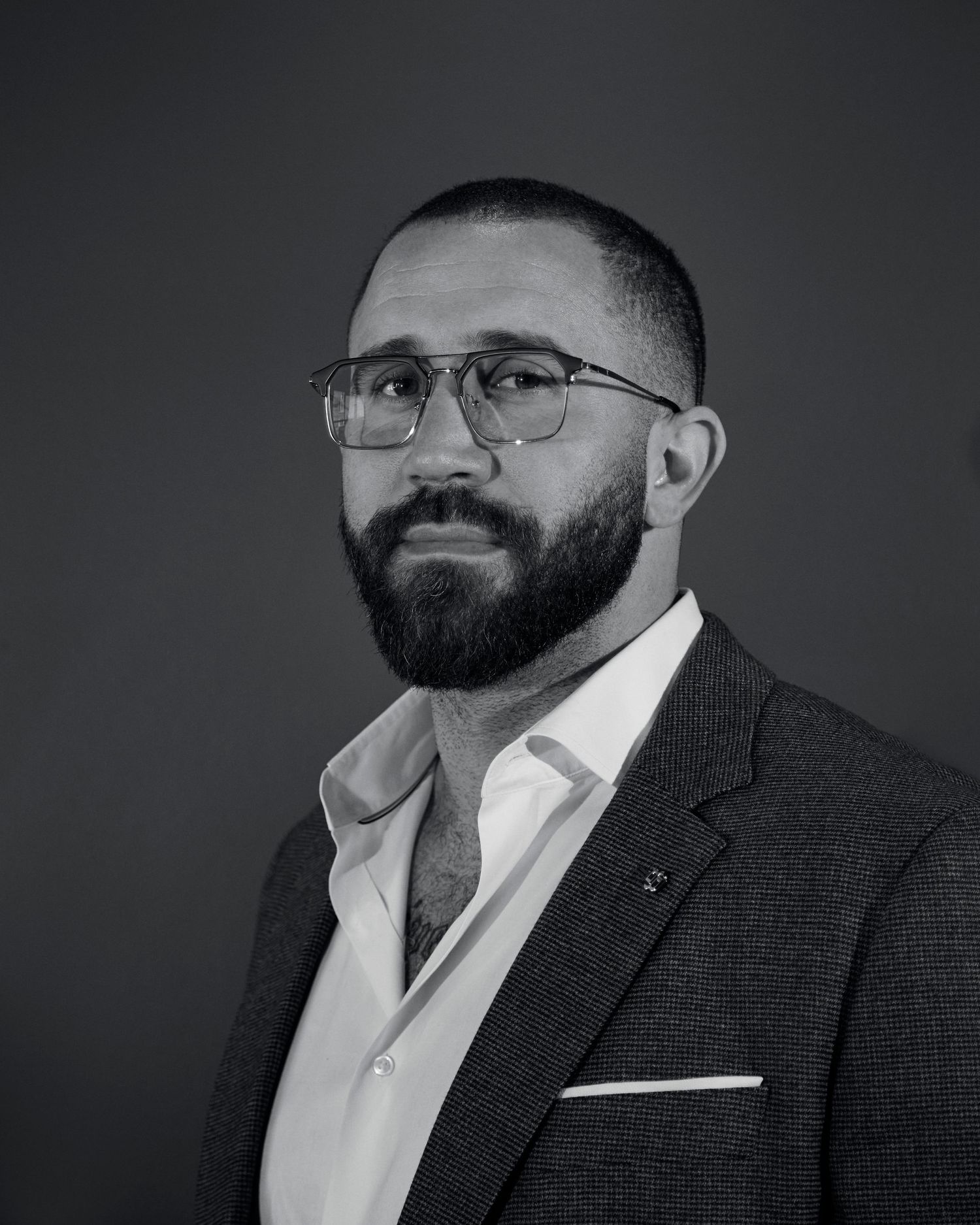 Professional headshot of a bearded man in business attire against a dark background.