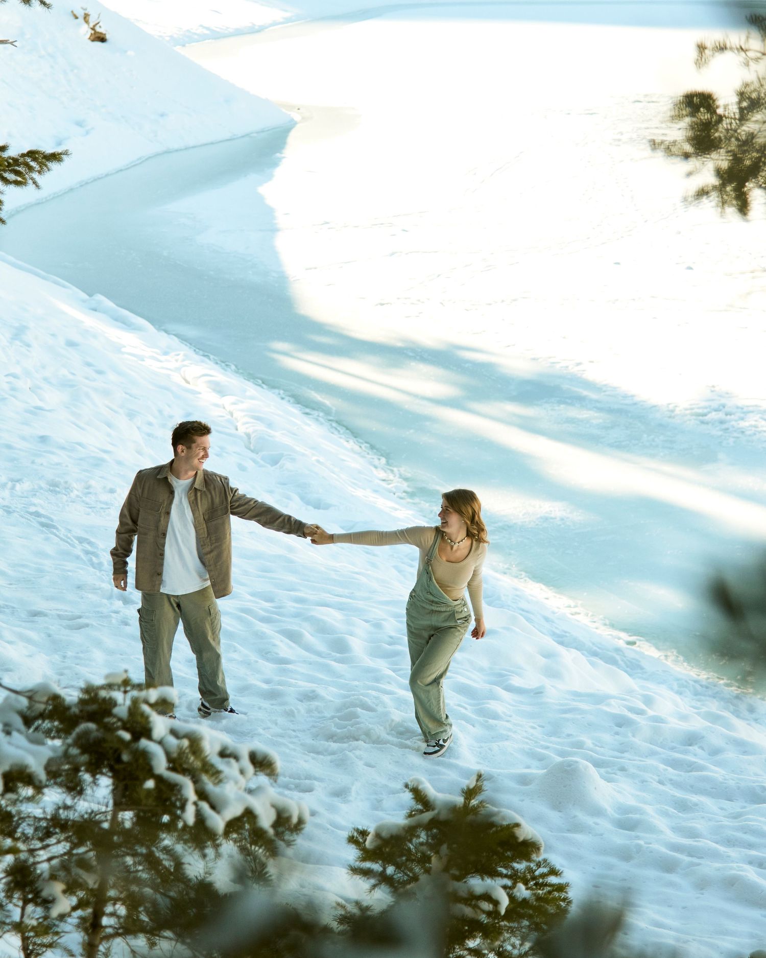 Couple holding hands while walking through snowy landscape with mountain views.