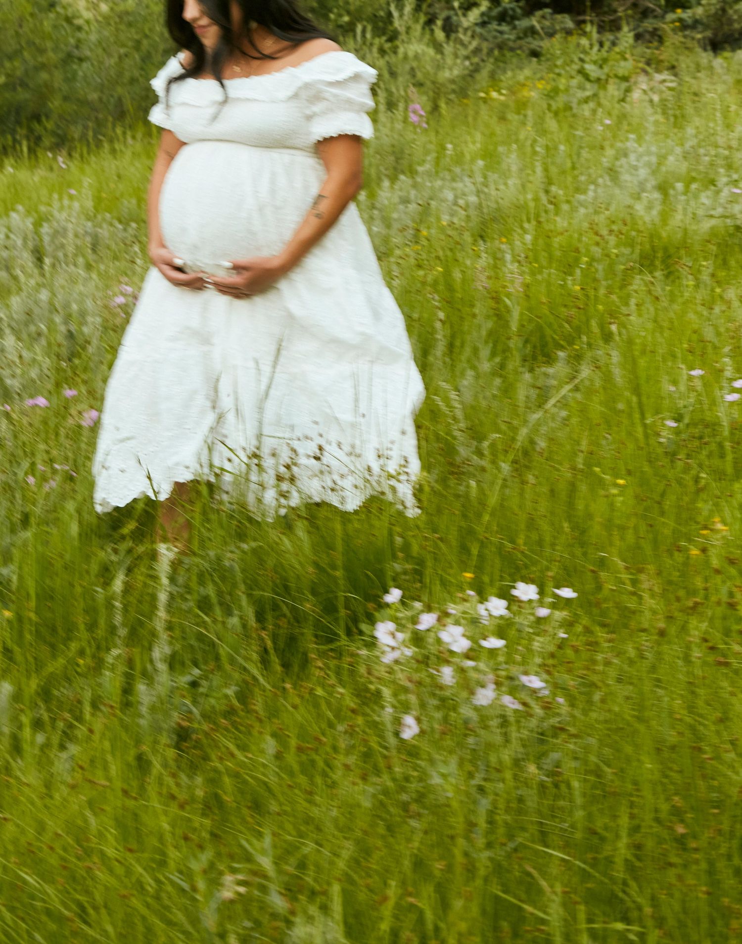 Detail shot of a white eyelet lace maternity dress against green mountain wildflowers.
