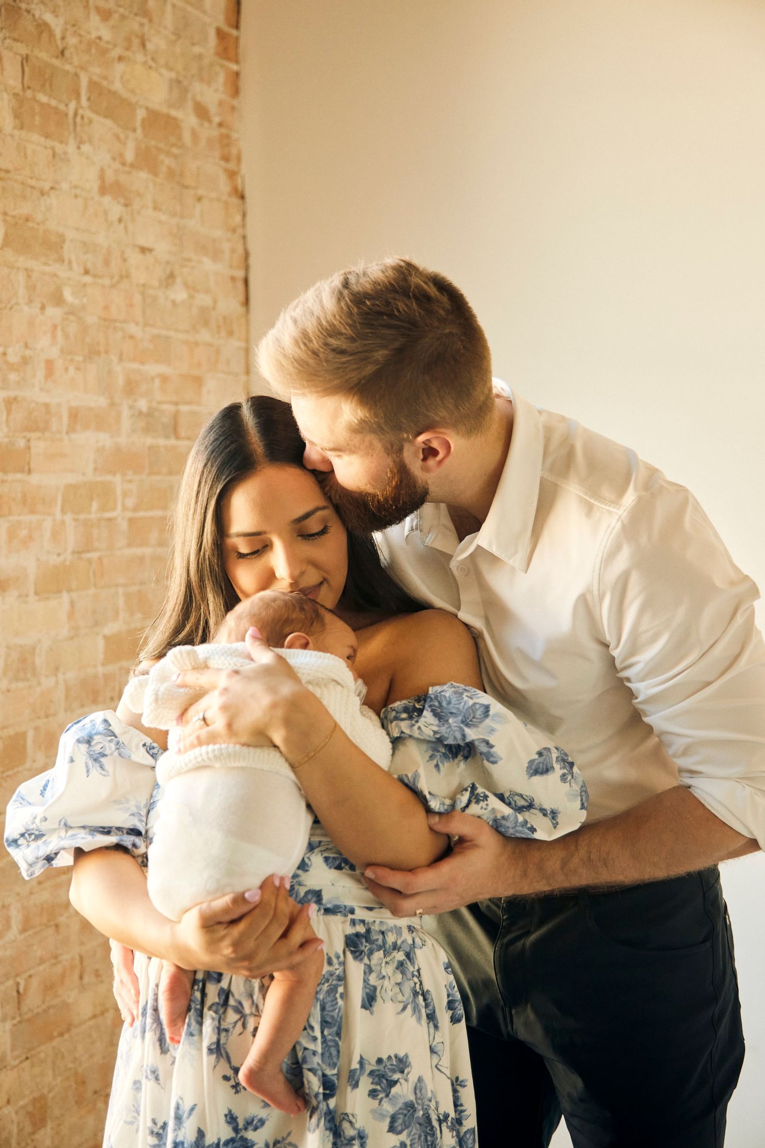 Intimate family portrait with newborn baby against brick wall in natural light.
