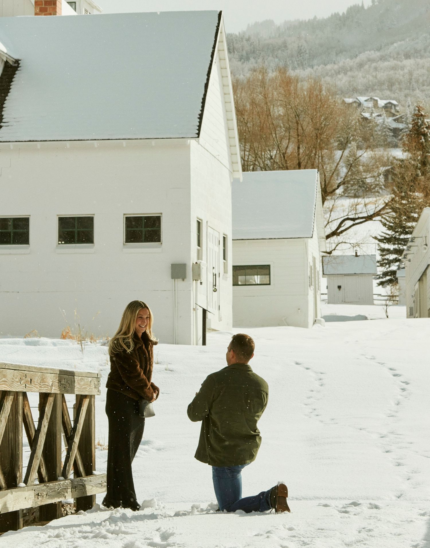 A romantic moment unfolds between two people outside white buildings in a snow-covered mountain setting.
