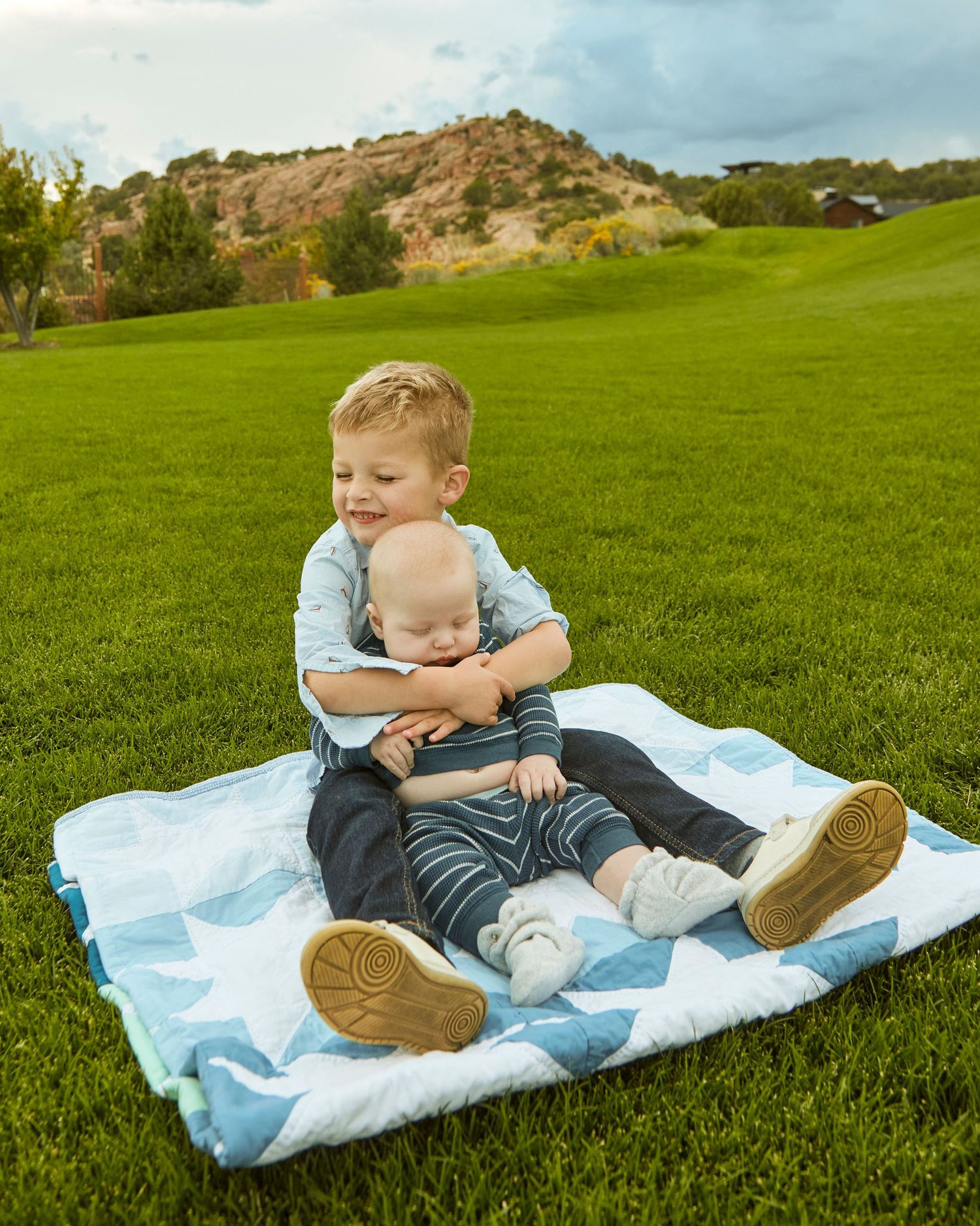 Two children sitting on blue blanket in lush green grass.