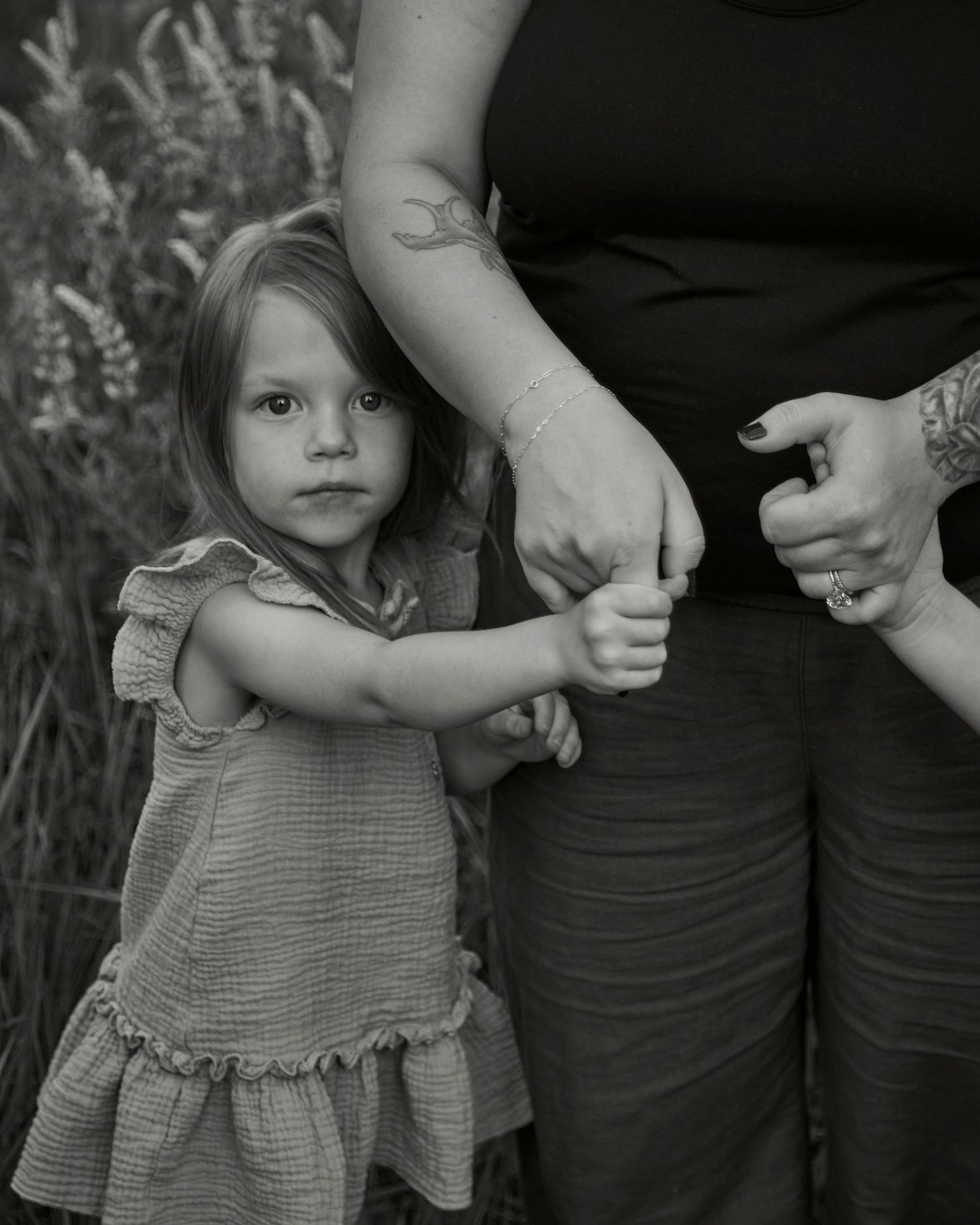 Black and white portrait showing small child holding hands with adults outdoors.