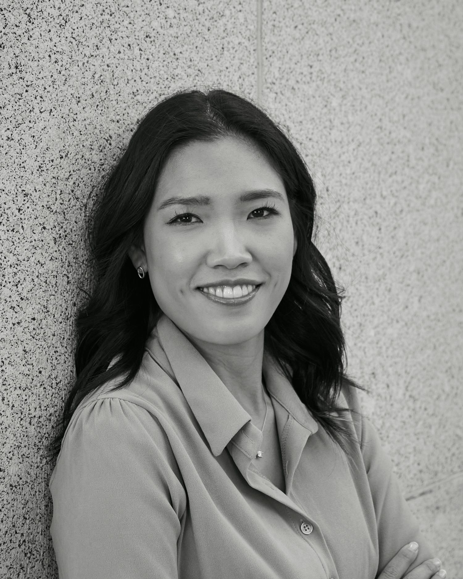 Professional black and white portrait of a woman in business attire against a textured wall.