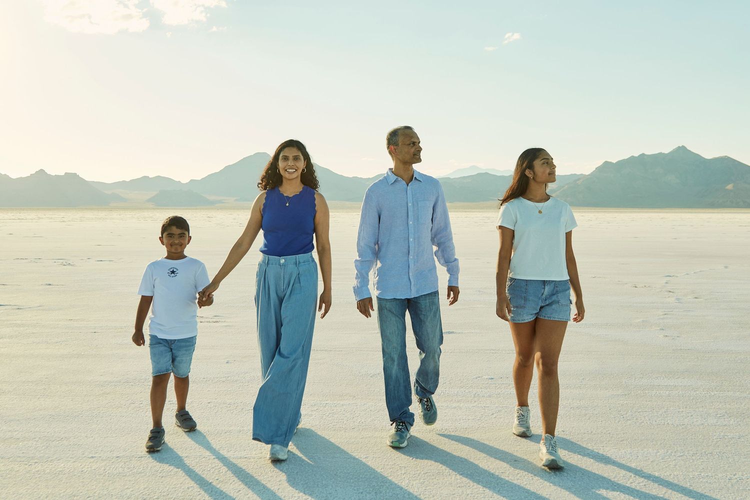 Family of four walking together across white salt flats with mountains in background.