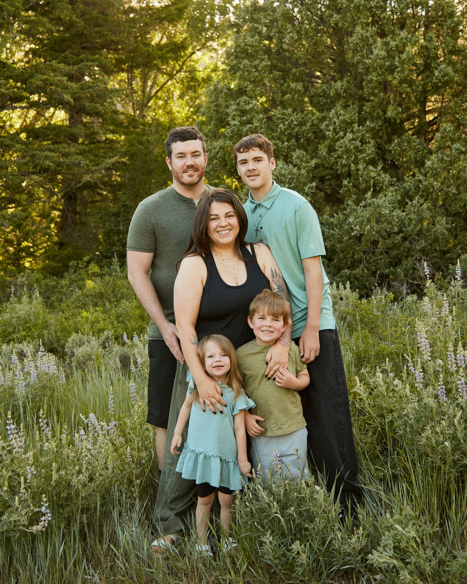 A family stands together in a field of wildflowers at sunset with trees in the background.