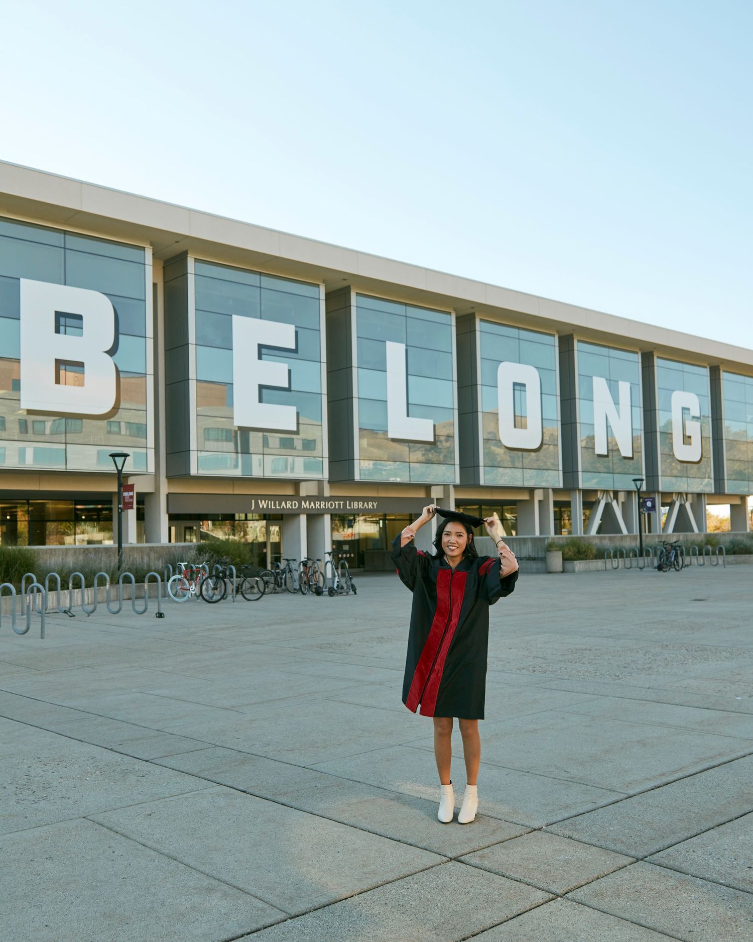 A figure poses enthusiastically in front of large BELONG signage on a modern building facade.