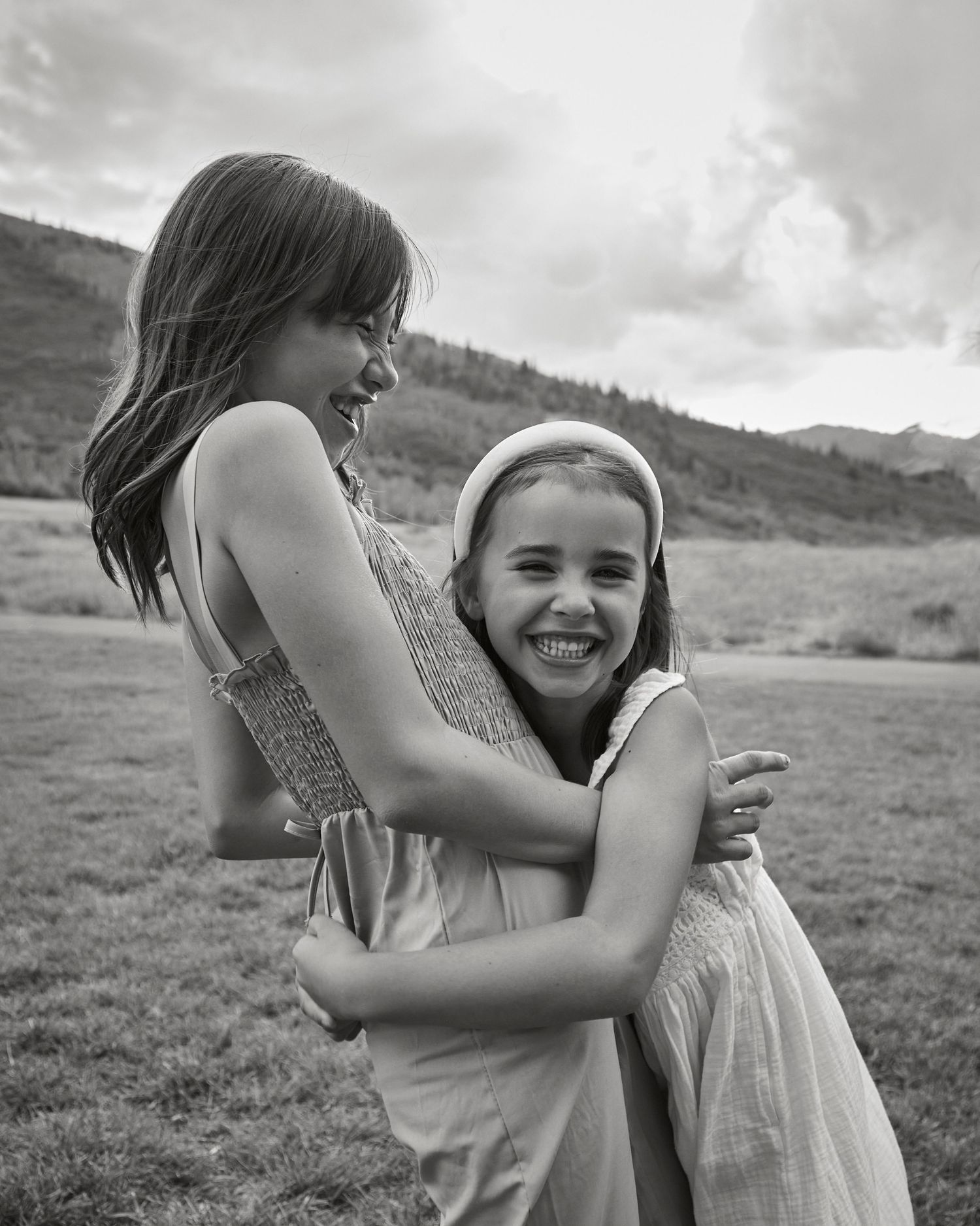 Two young friends sharing a candid black and white moment outdoors in a mountain field.