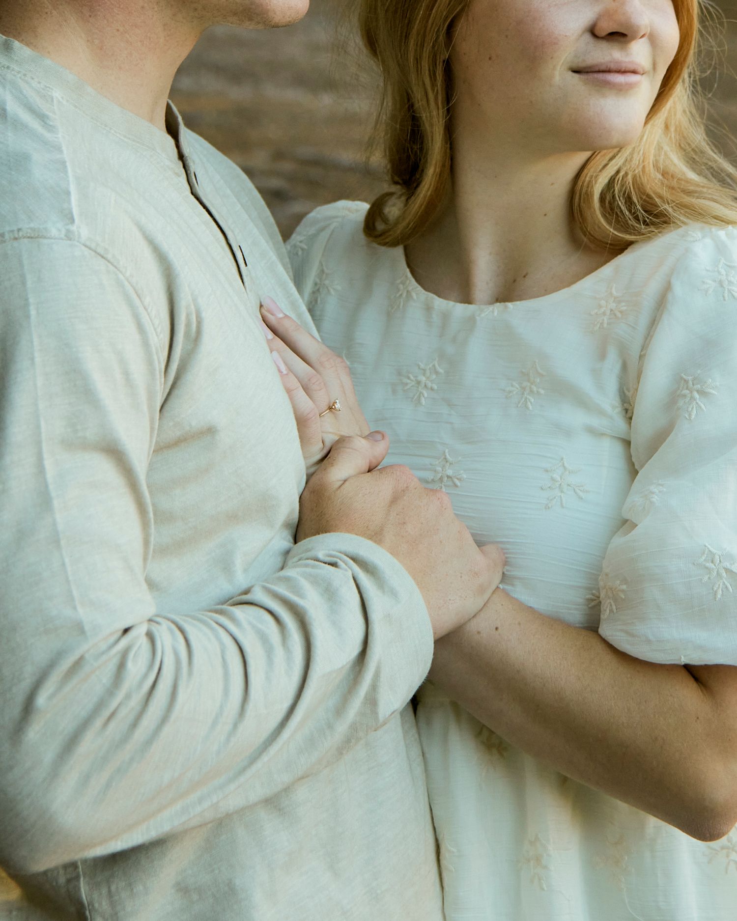 A gentle embrace captured in soft lighting showing interlocked hands and white clothing.