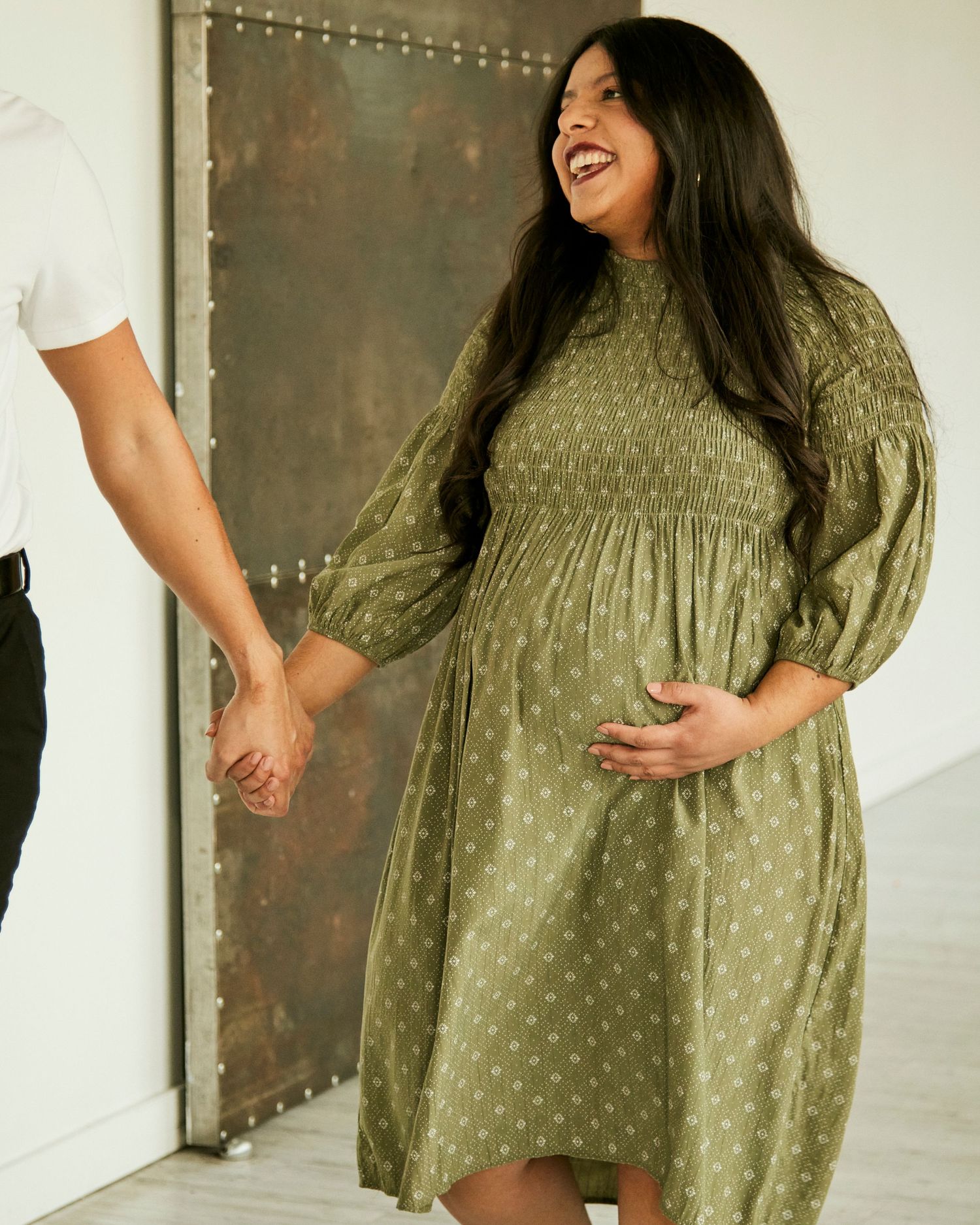 Person in sage green polka dot dress laughing while holding hands.