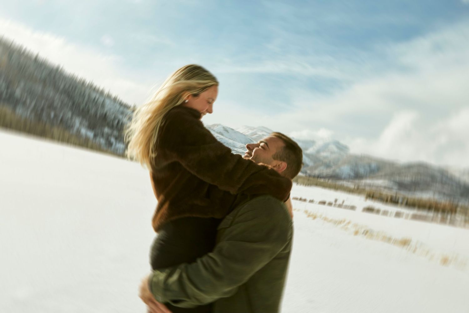 Happy couple embracing in winter wonderland with snow-capped mountains in background.