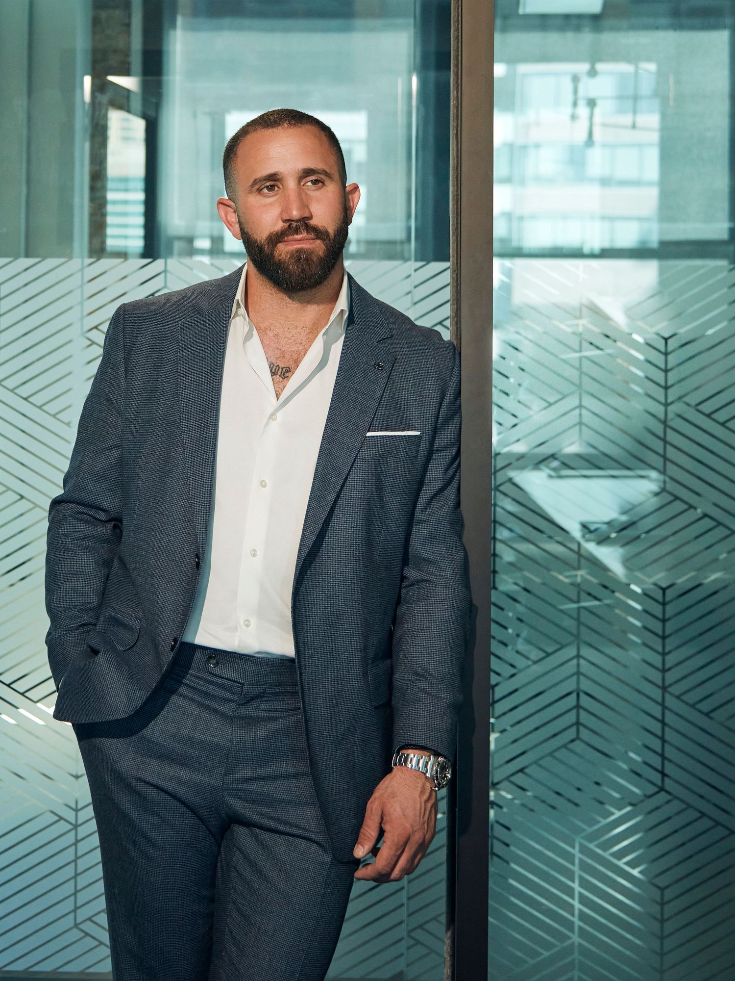 Professional poses in business attire against geometric patterned glass wall in modern office setting.
