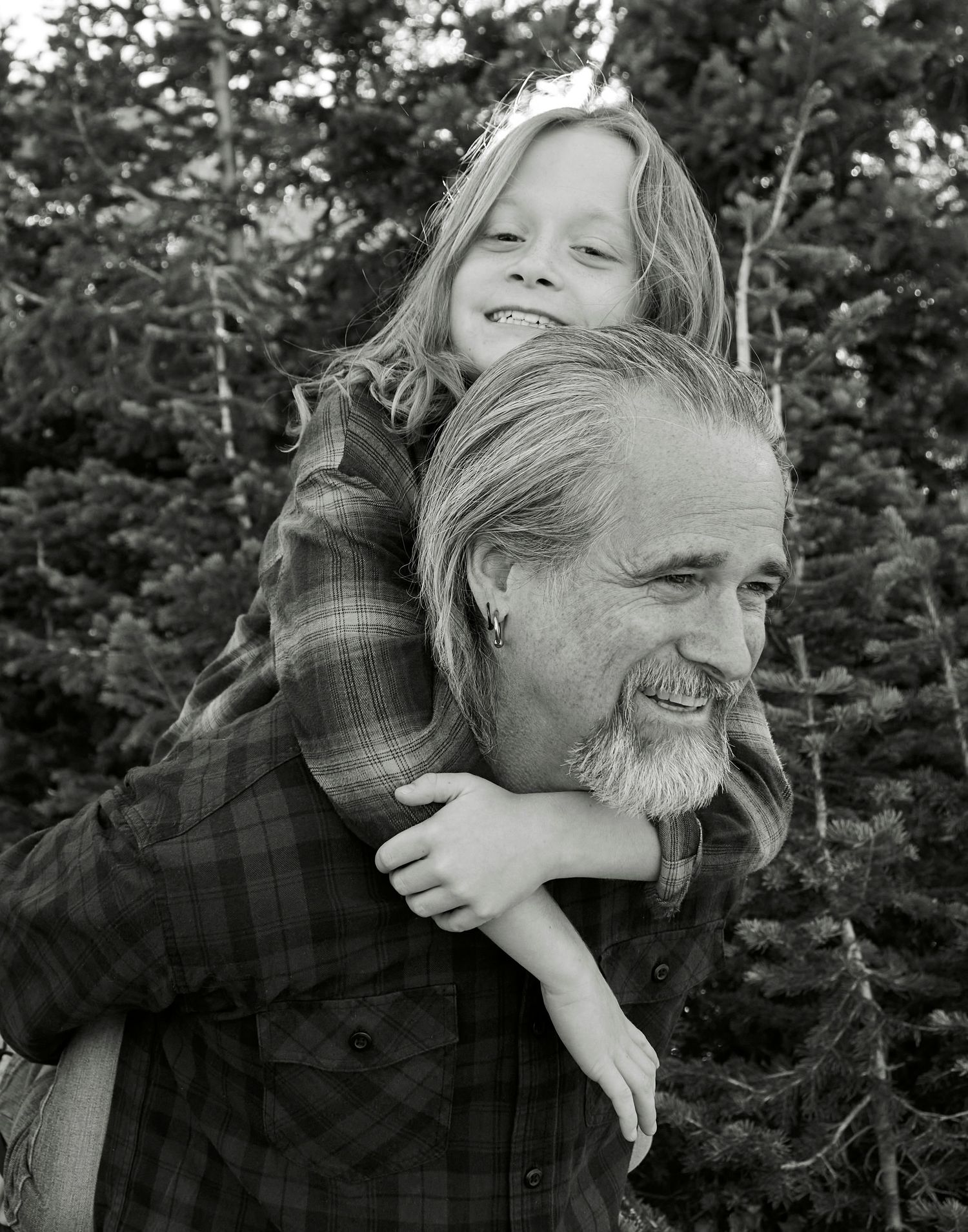 Black and white portrait of a playful piggyback ride among pine trees.