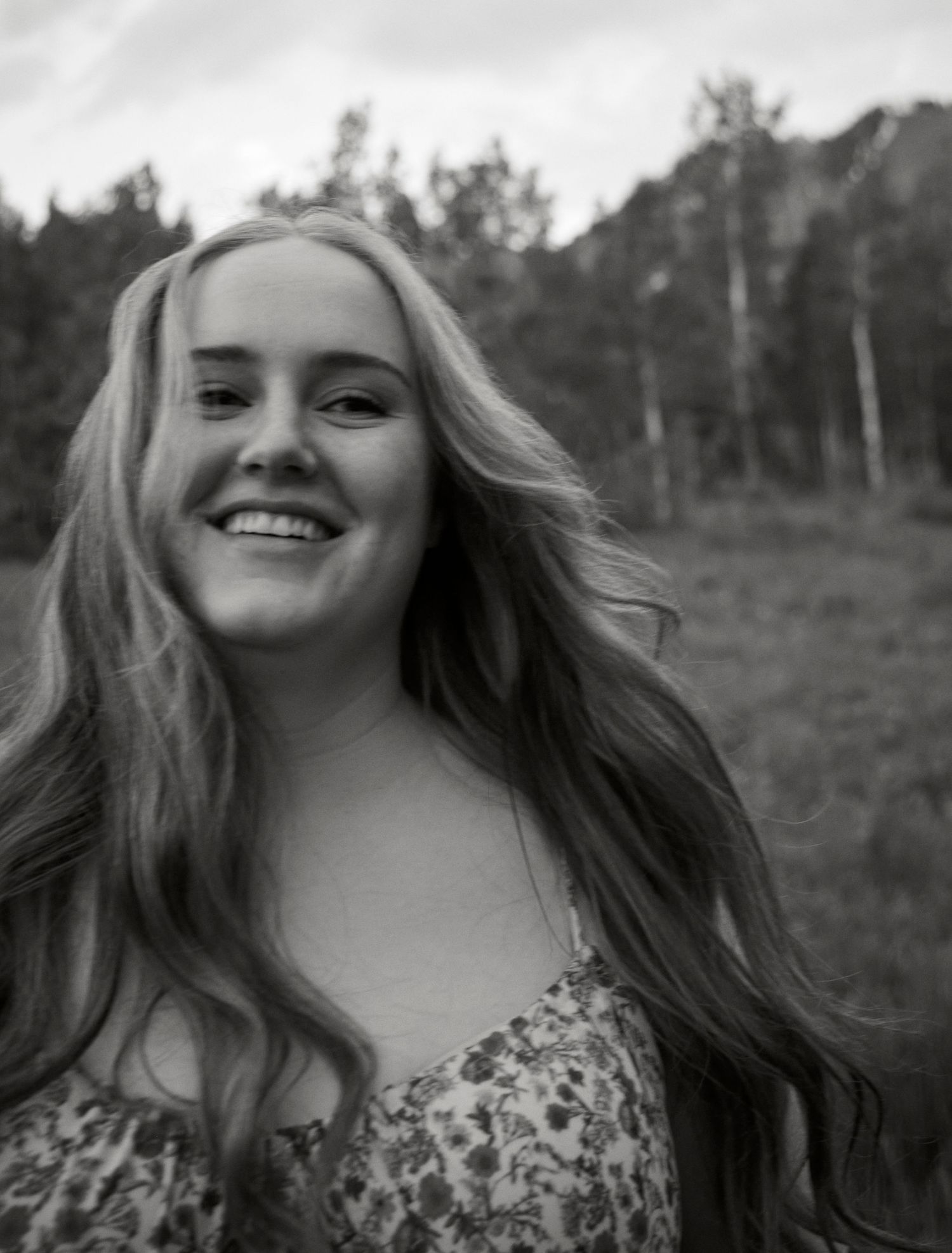 A black and white portrait showing a joyful expression with long wavy hair and a floral top.