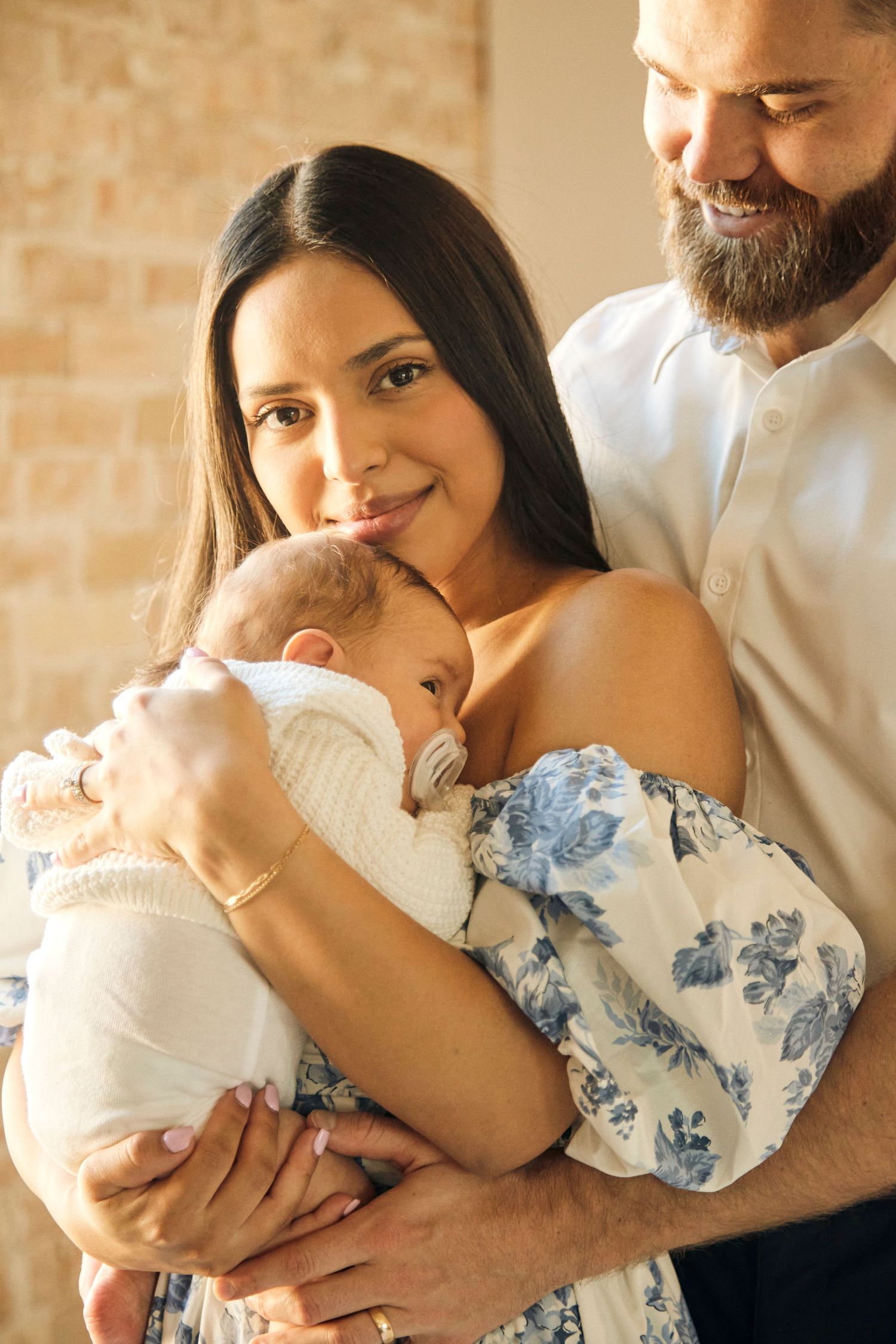 Tender family moment with newborn baby against exposed brick wall in warm lighting.