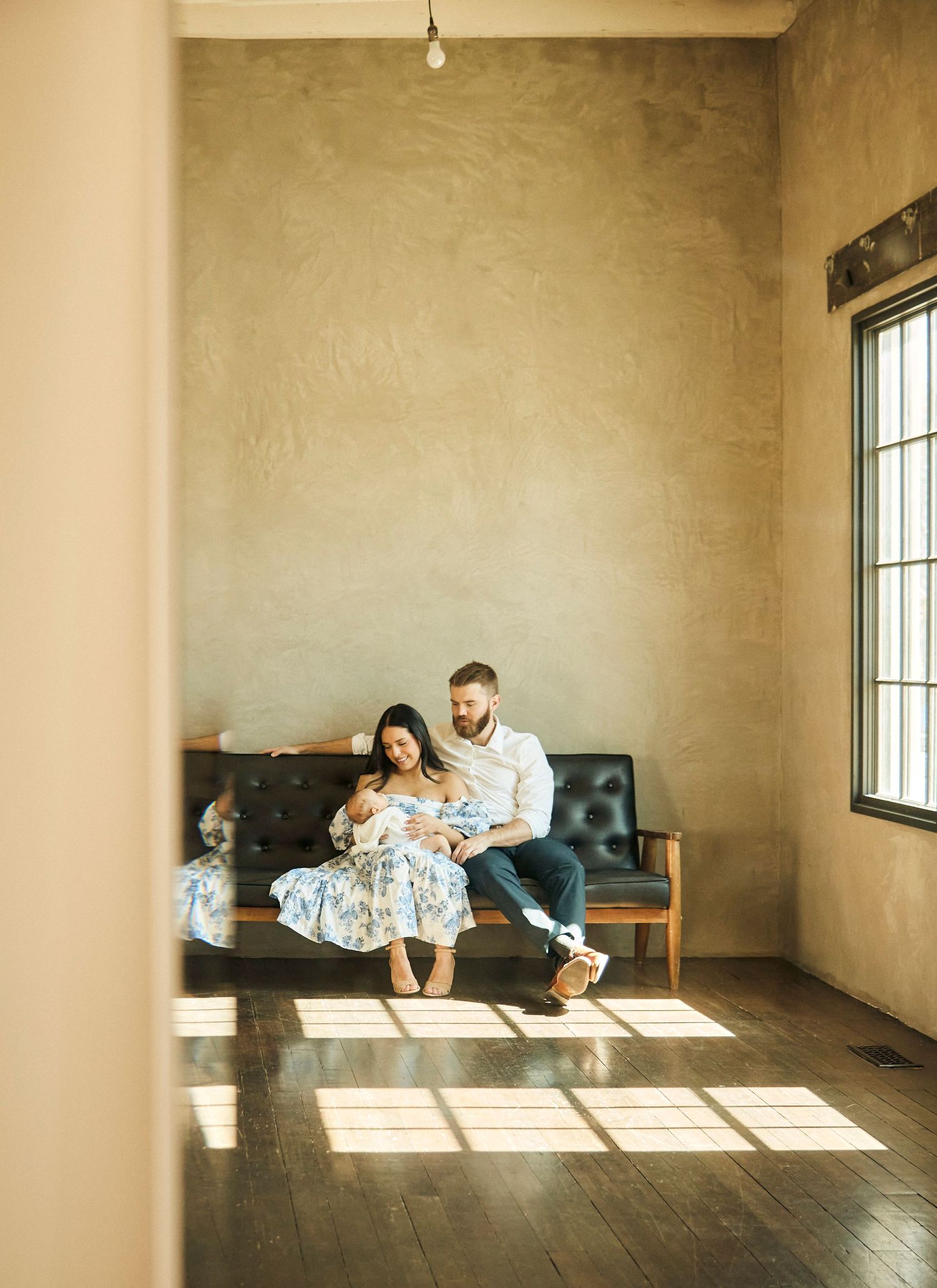 Family sits together on vintage couch as sunlight streams through windows in minimalist room.