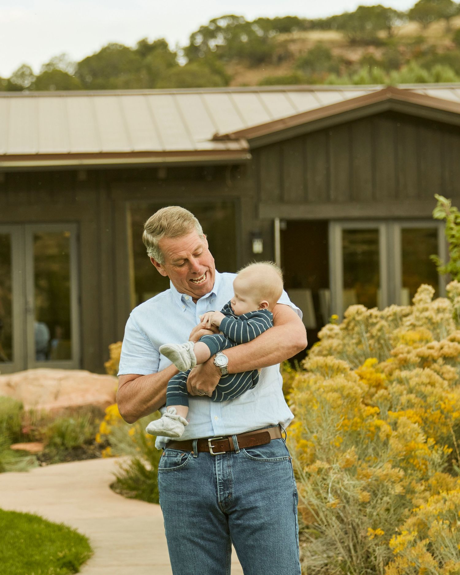 Tender moment outdoors with baby near rustic house and yellow flowers.