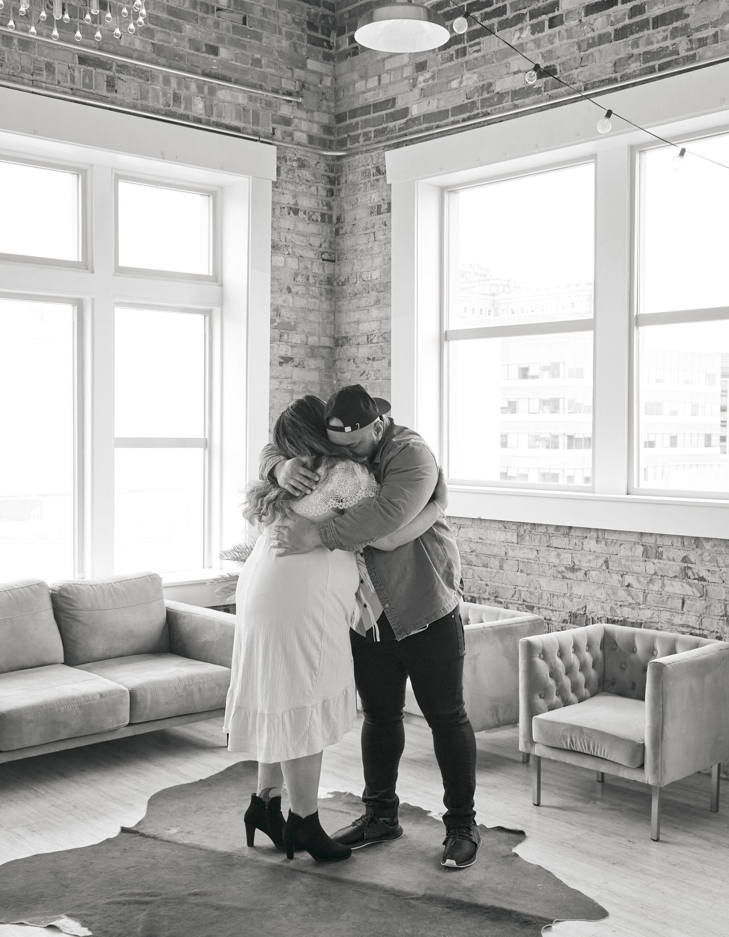 A romantic embrace captured in black and white in an urban loft setting with exposed brick walls.