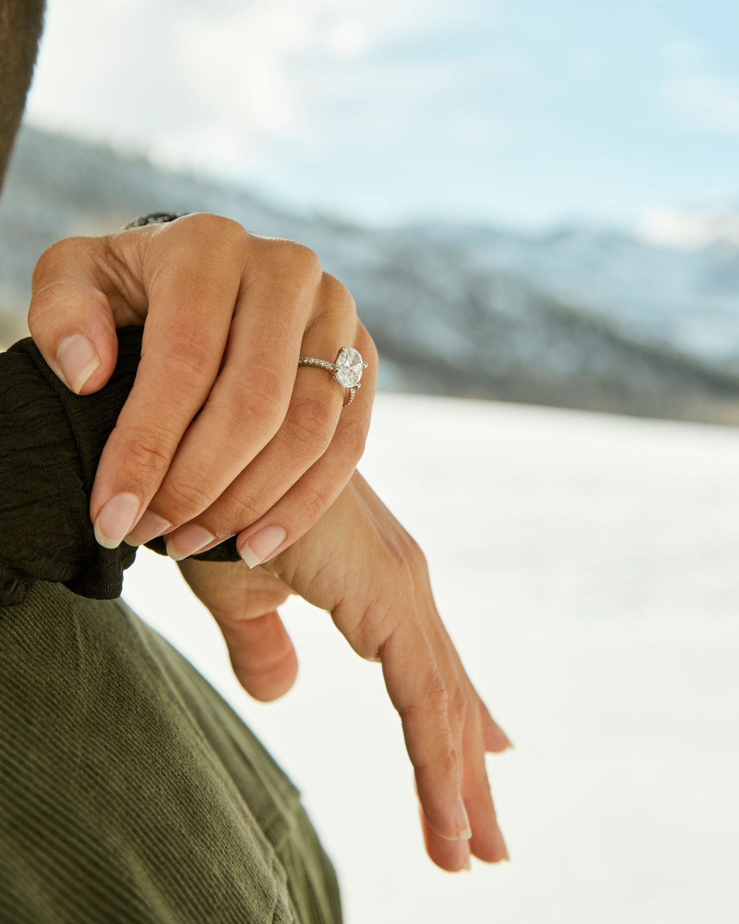 Close-up of engagement ring on hand with snowy mountain backdrop.