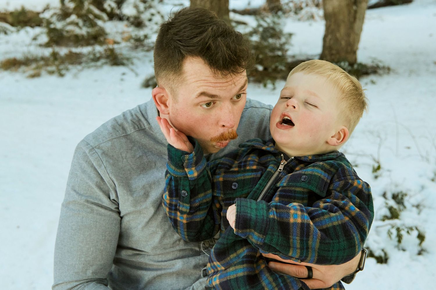 Parent and child share playful expressions in winter setting wearing plaid and grey.