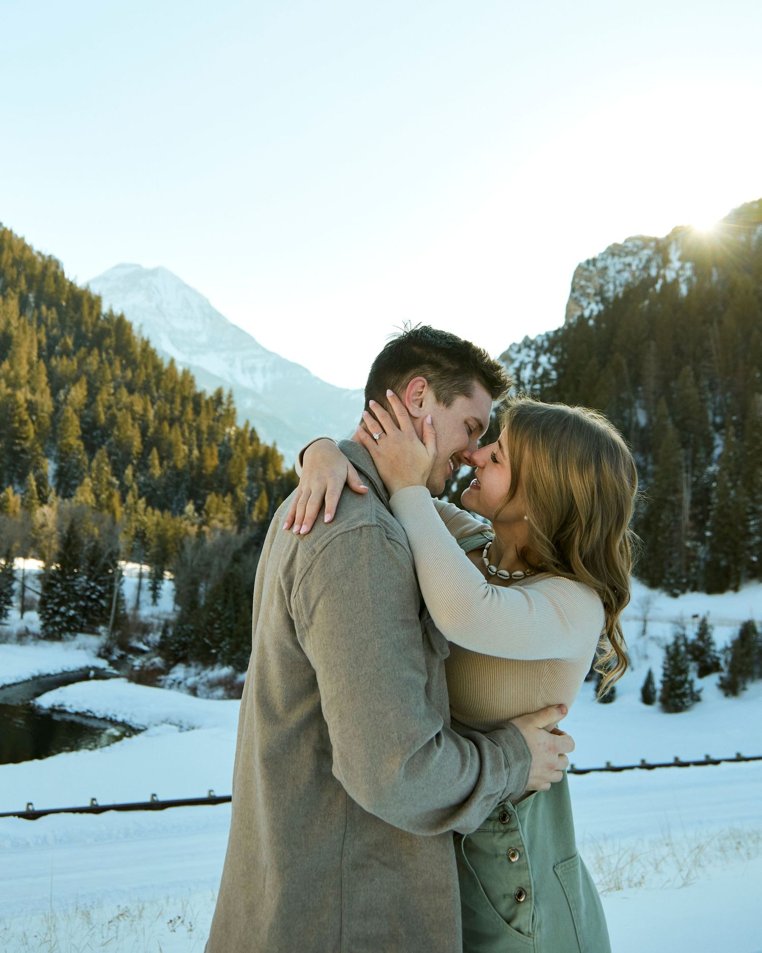Tender moment between couple embracing in snowy mountain setting with golden sunlight.