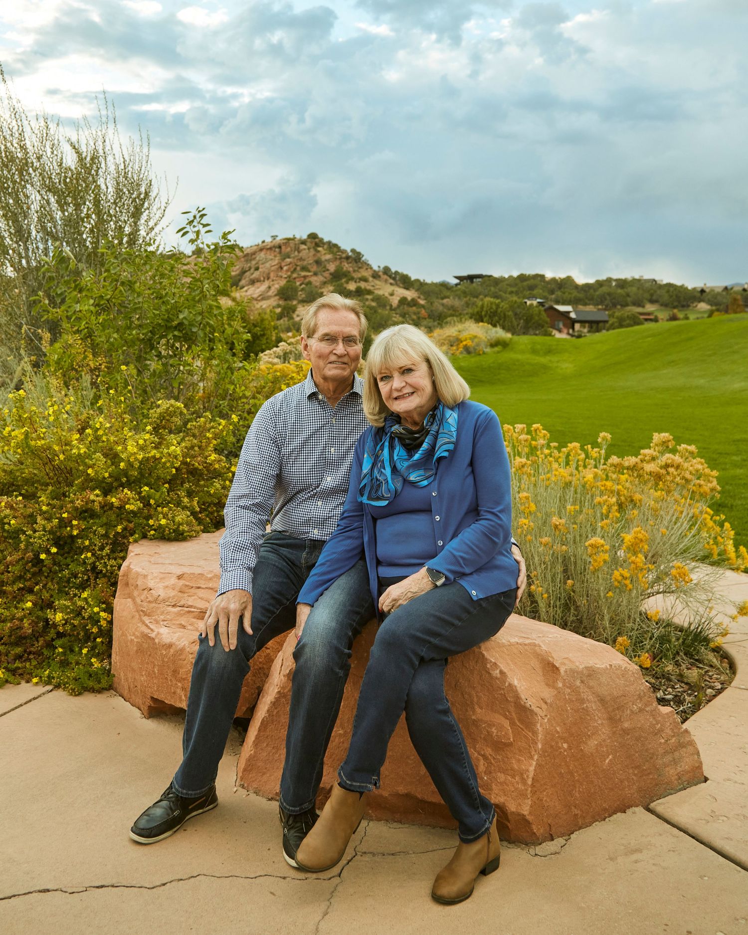 Couple sitting together on large red rock with mountain landscape in background.