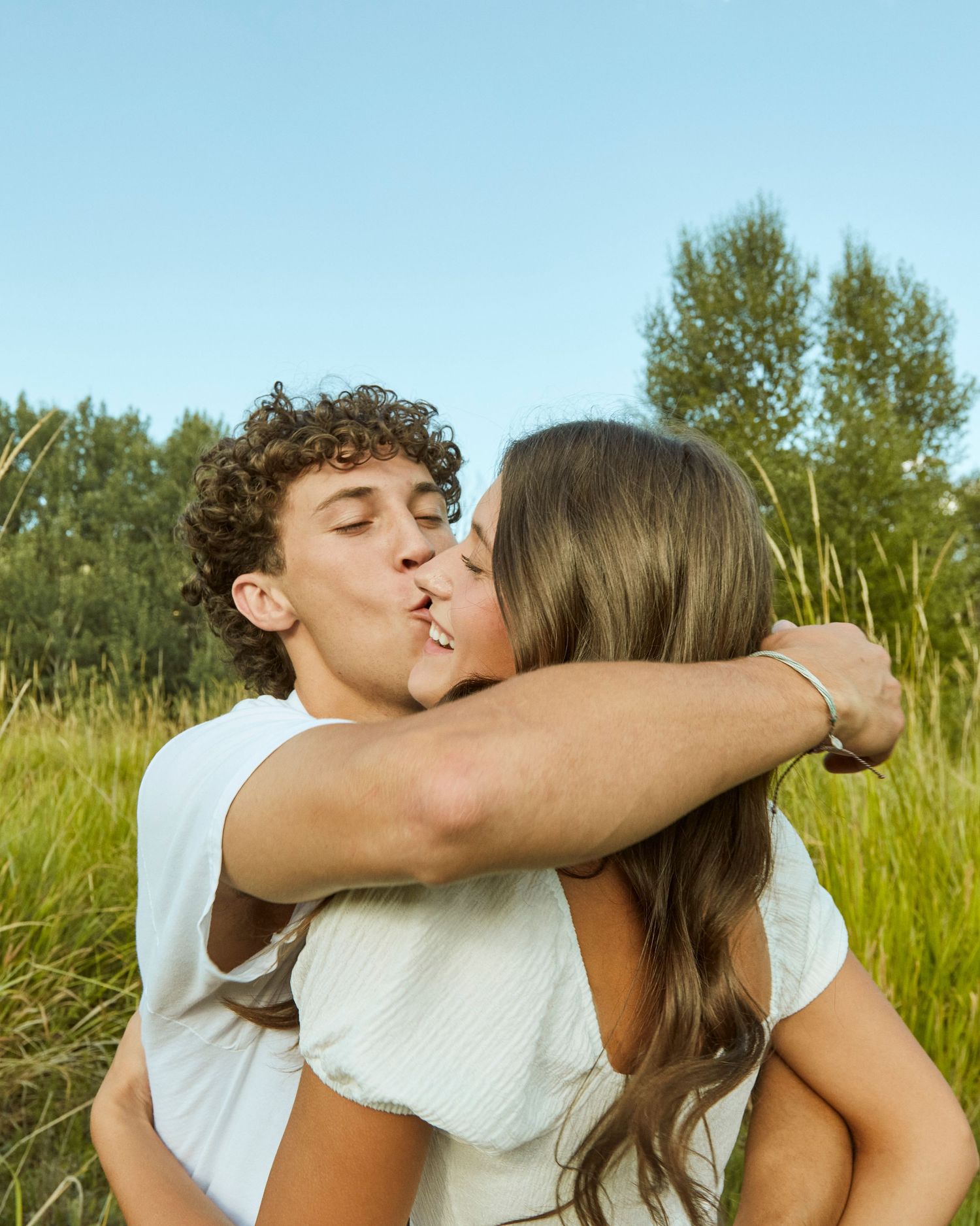 Summer portrait of couple sharing a passionate kiss in tall grass field.
