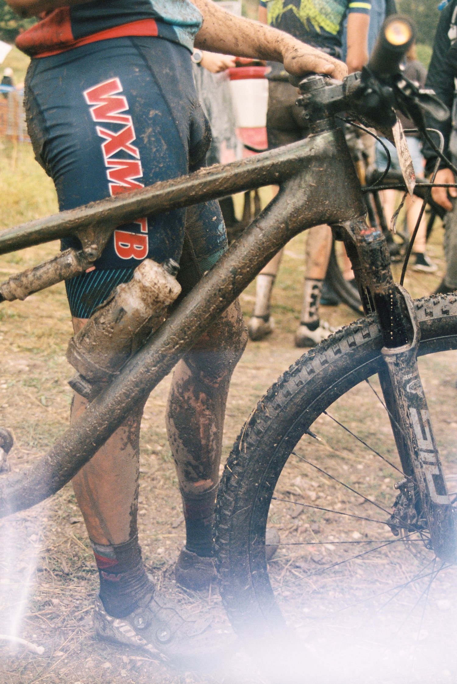 Muddy mountain bike frame and rider's legs showing wear from trail riding.