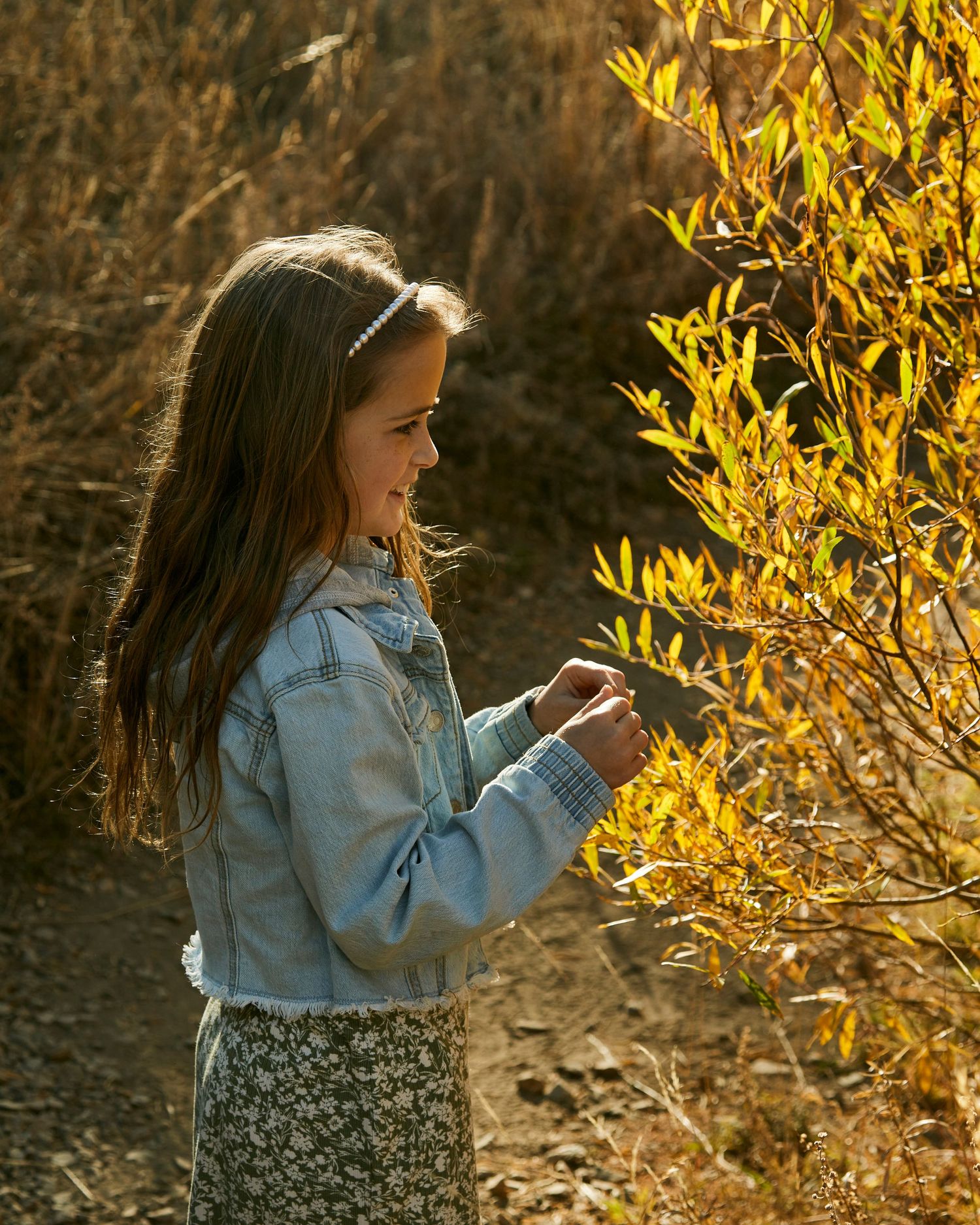 Person in denim jacket checking phone near golden foliage in natural light.