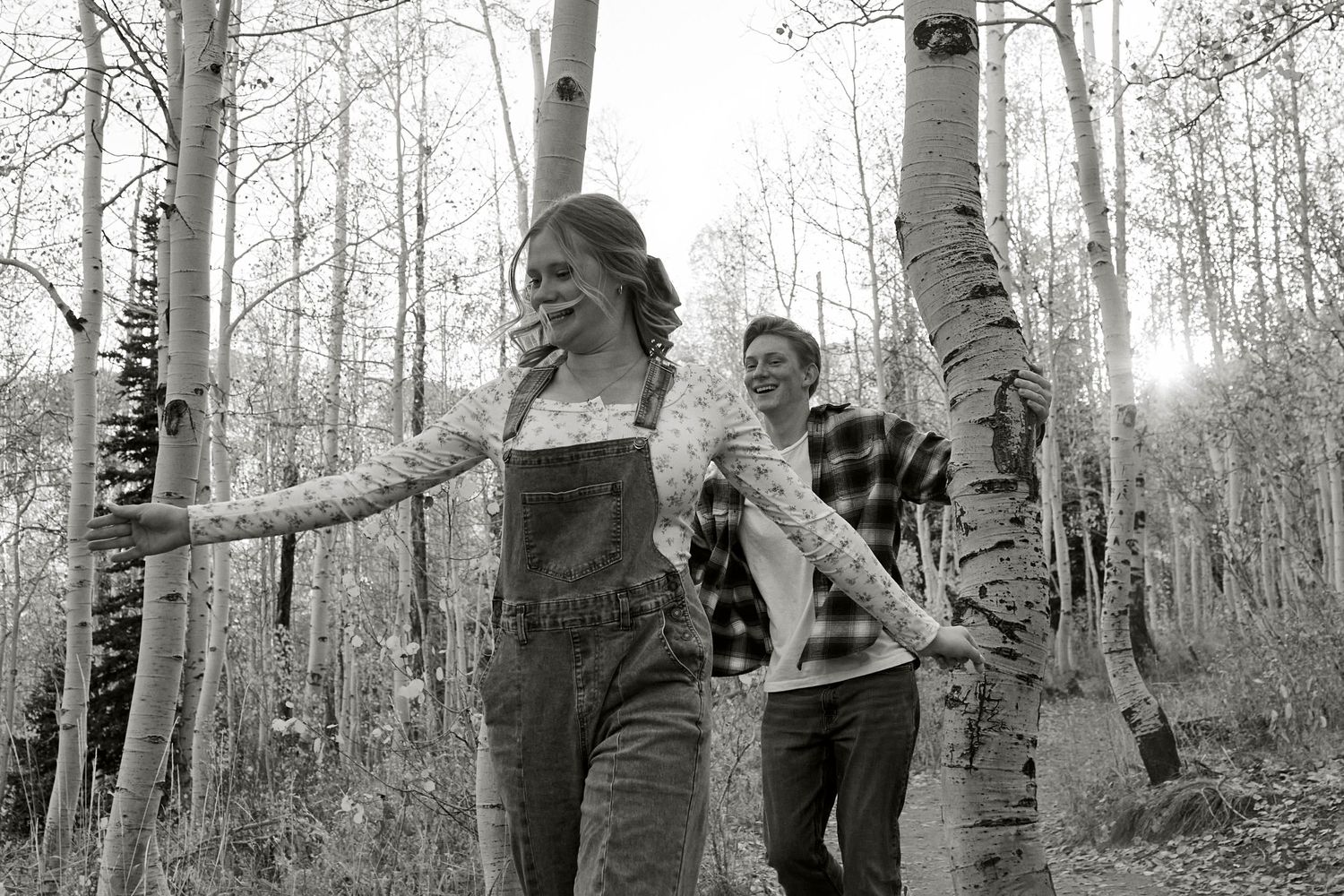 Black and white photo of couple playfully walking through an aspen grove.