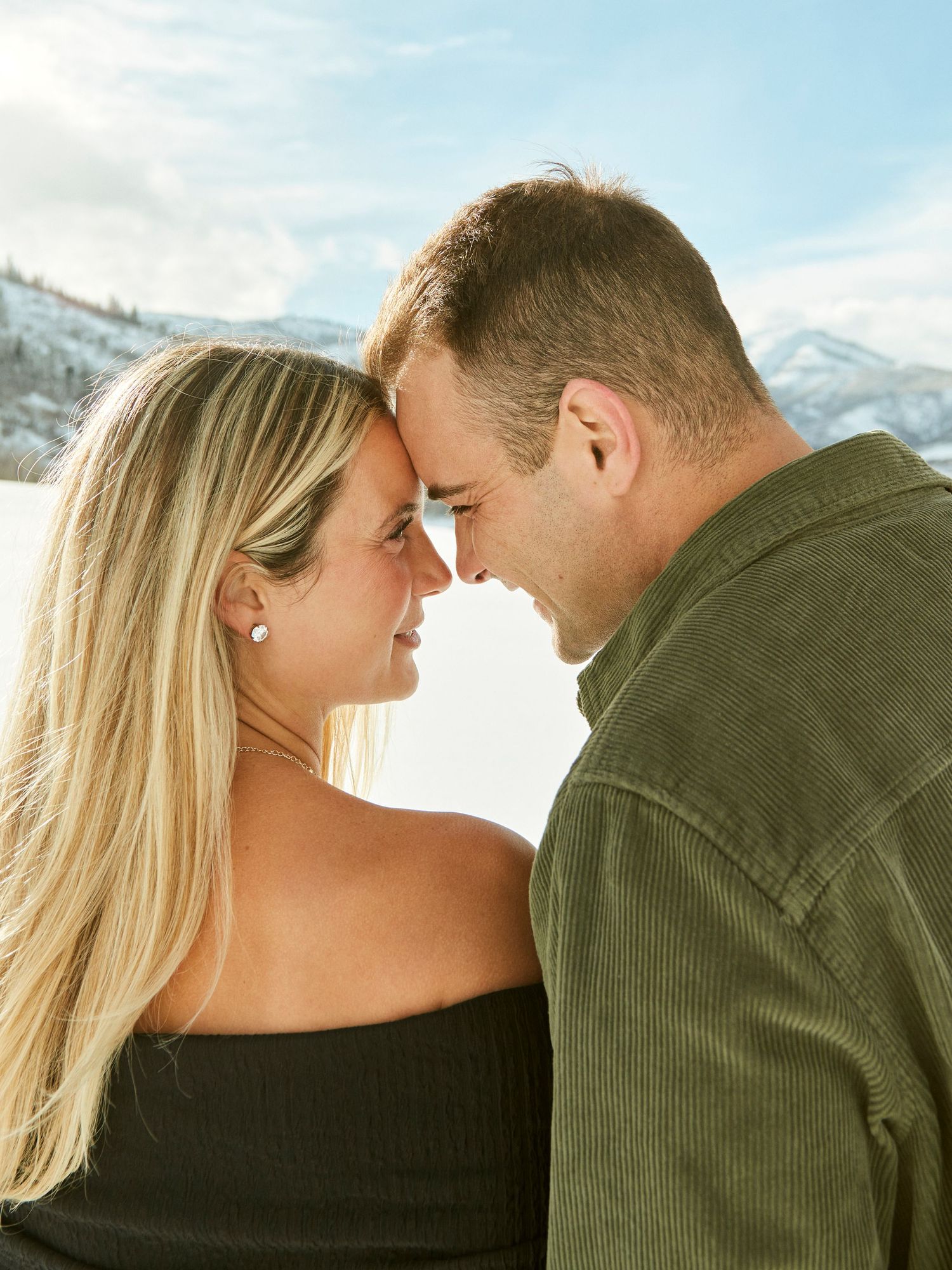 Intimate close-up of couple touching foreheads against snowy mountain backdrop.