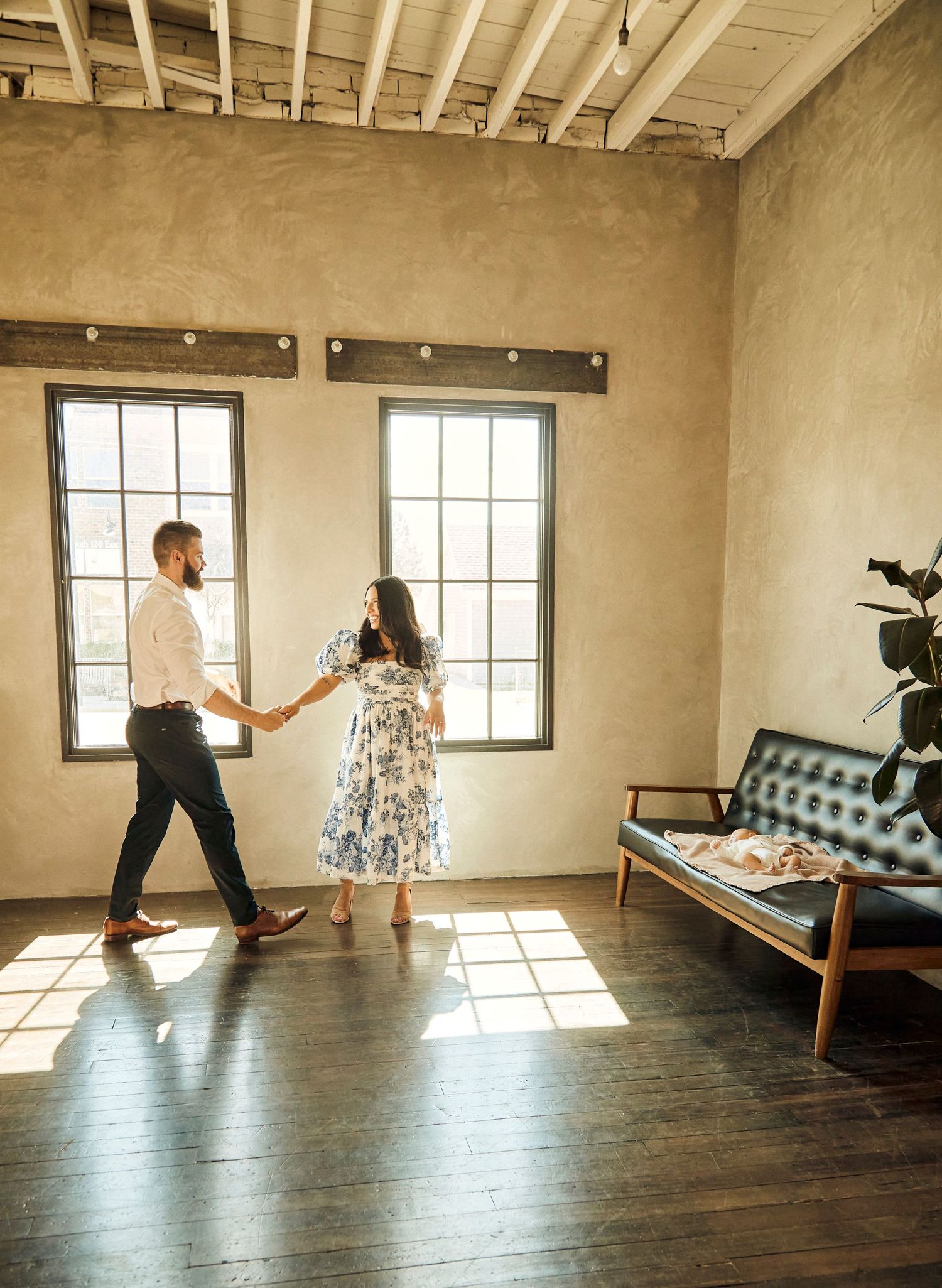 Couple dancing in sunlit room with hardwood floors and exposed brick walls.