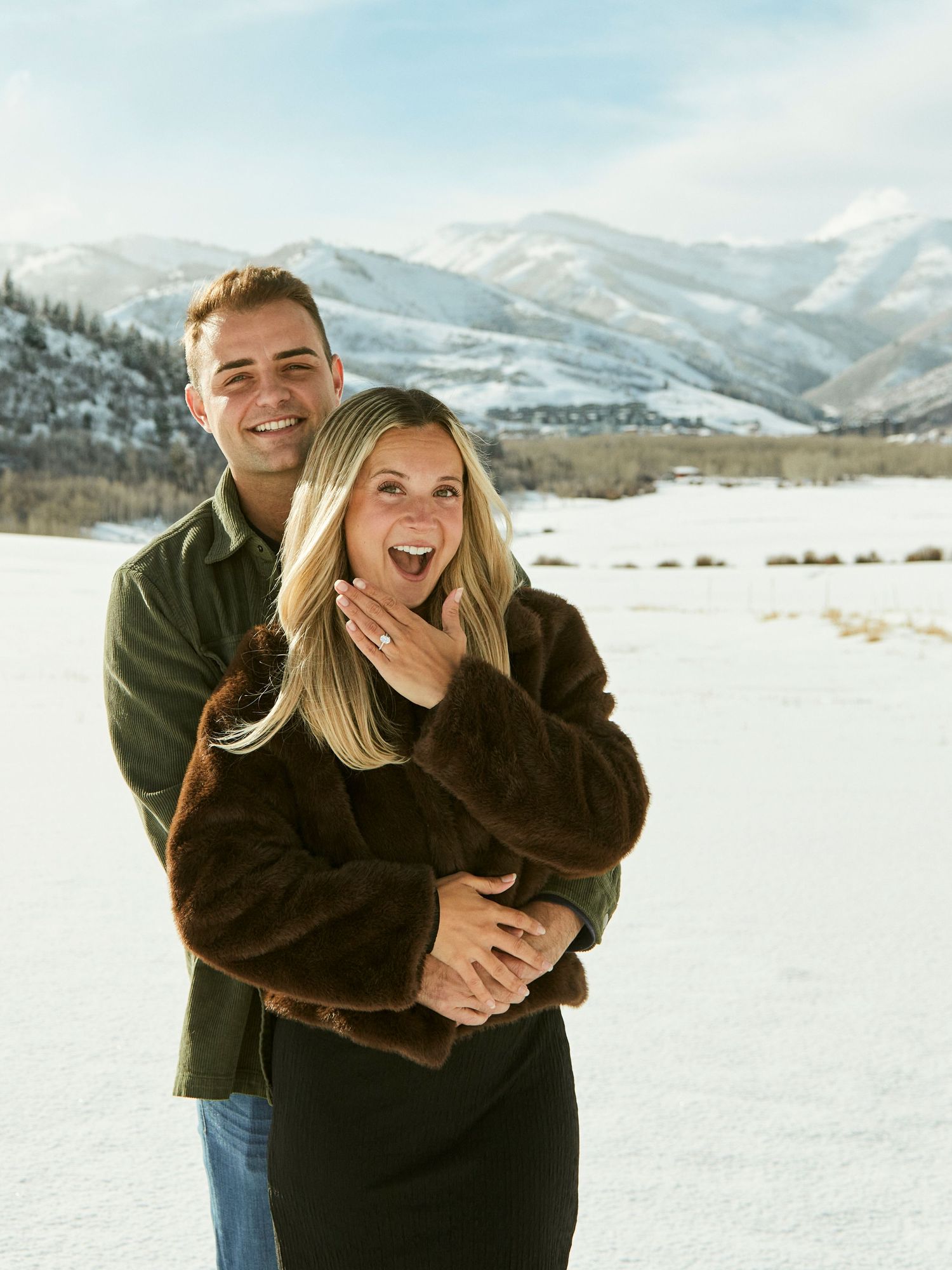 Joyful couple sharing a playful moment together in the snow with mountains in the background.