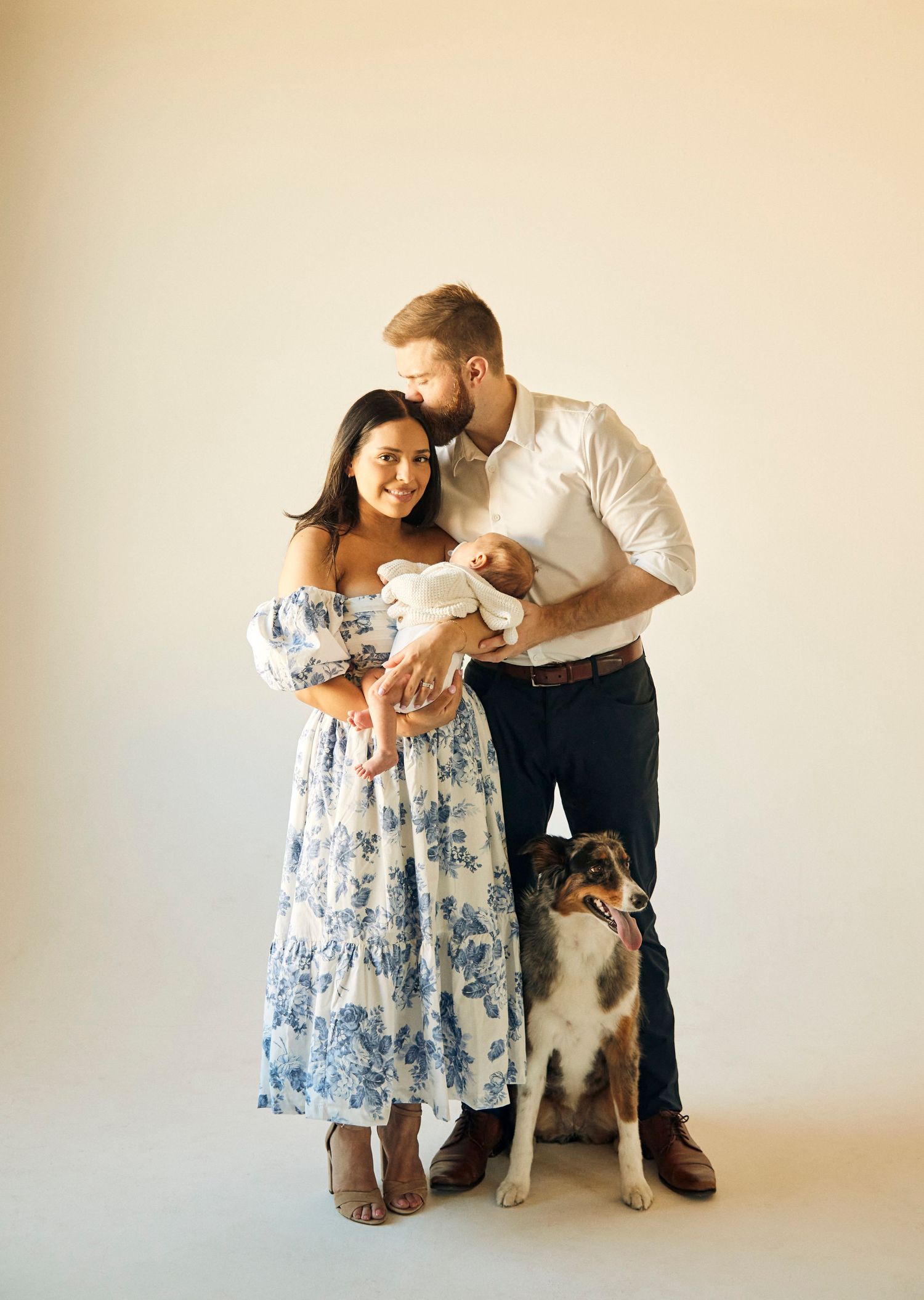 Intimate family moment with couple holding newborn baby while Australian shepherd sits beside them.