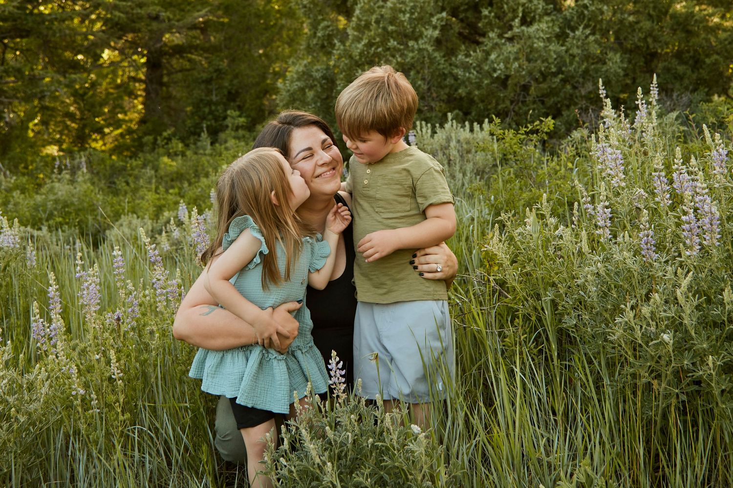 Three people share a joyful moment among wildflowers in a sunlit meadow.