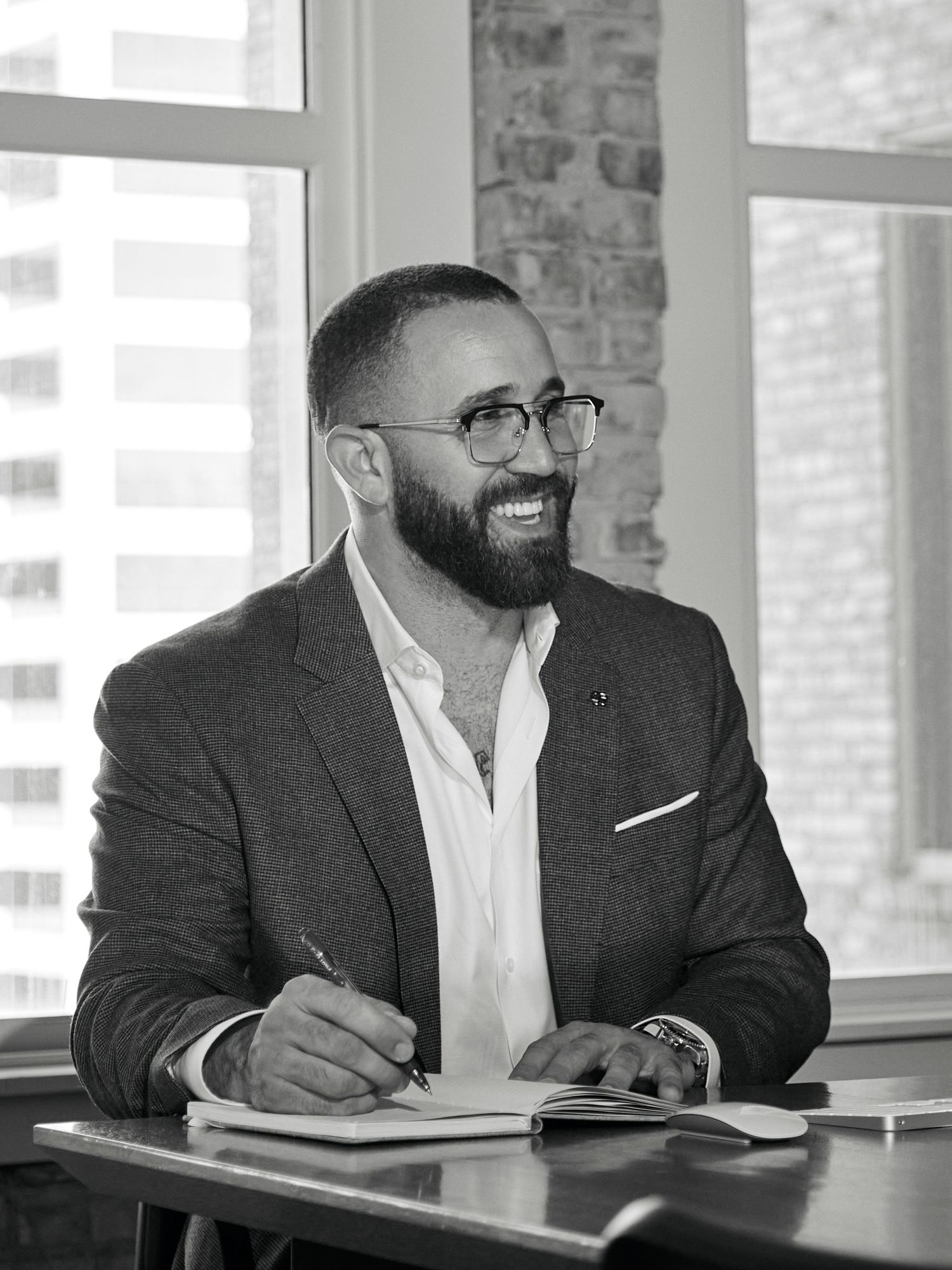 Business professional smiles while writing notes at modern office desk with natural lighting.