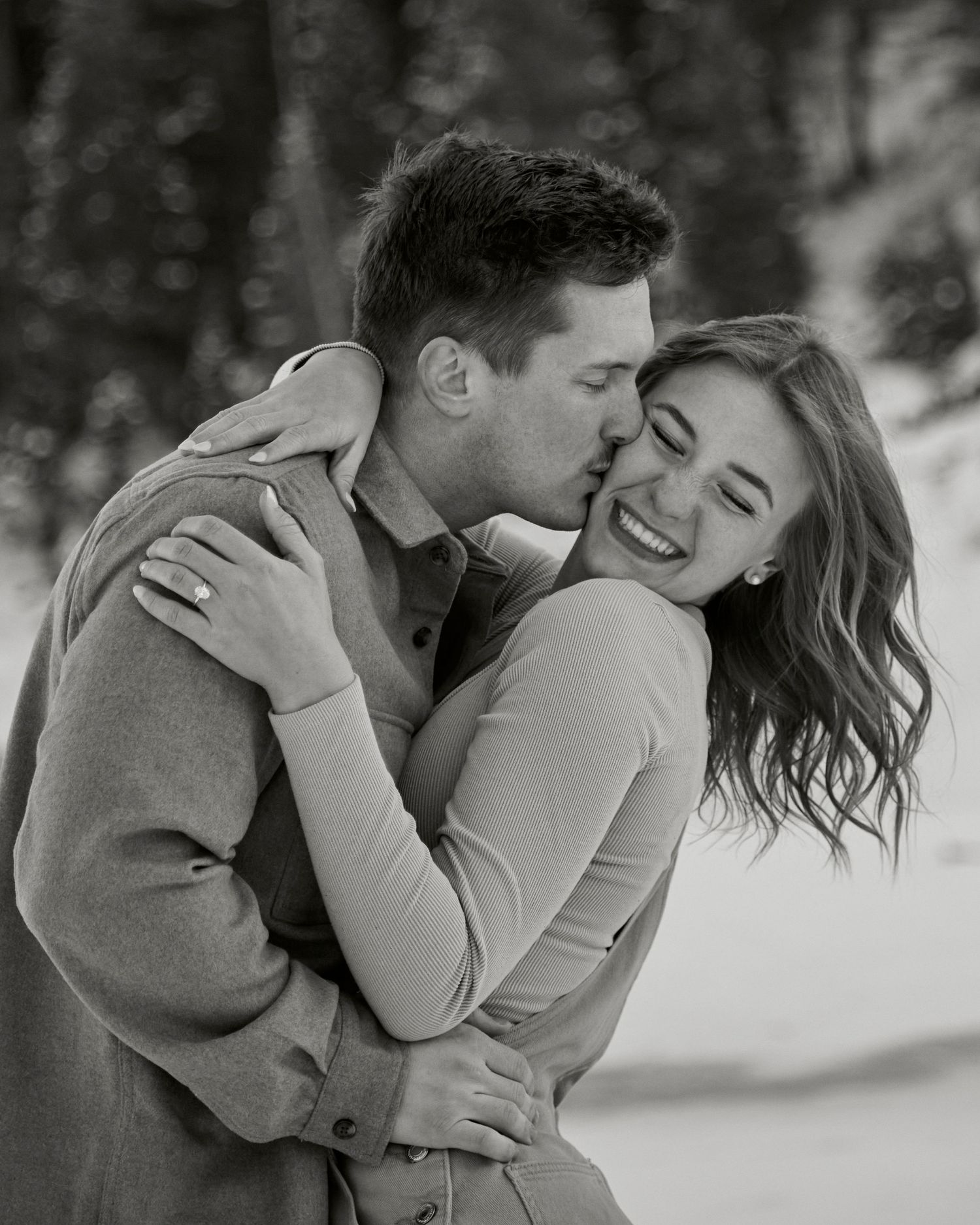 Intimate black and white portrait capturing a tender winter moment against snowy backdrop.