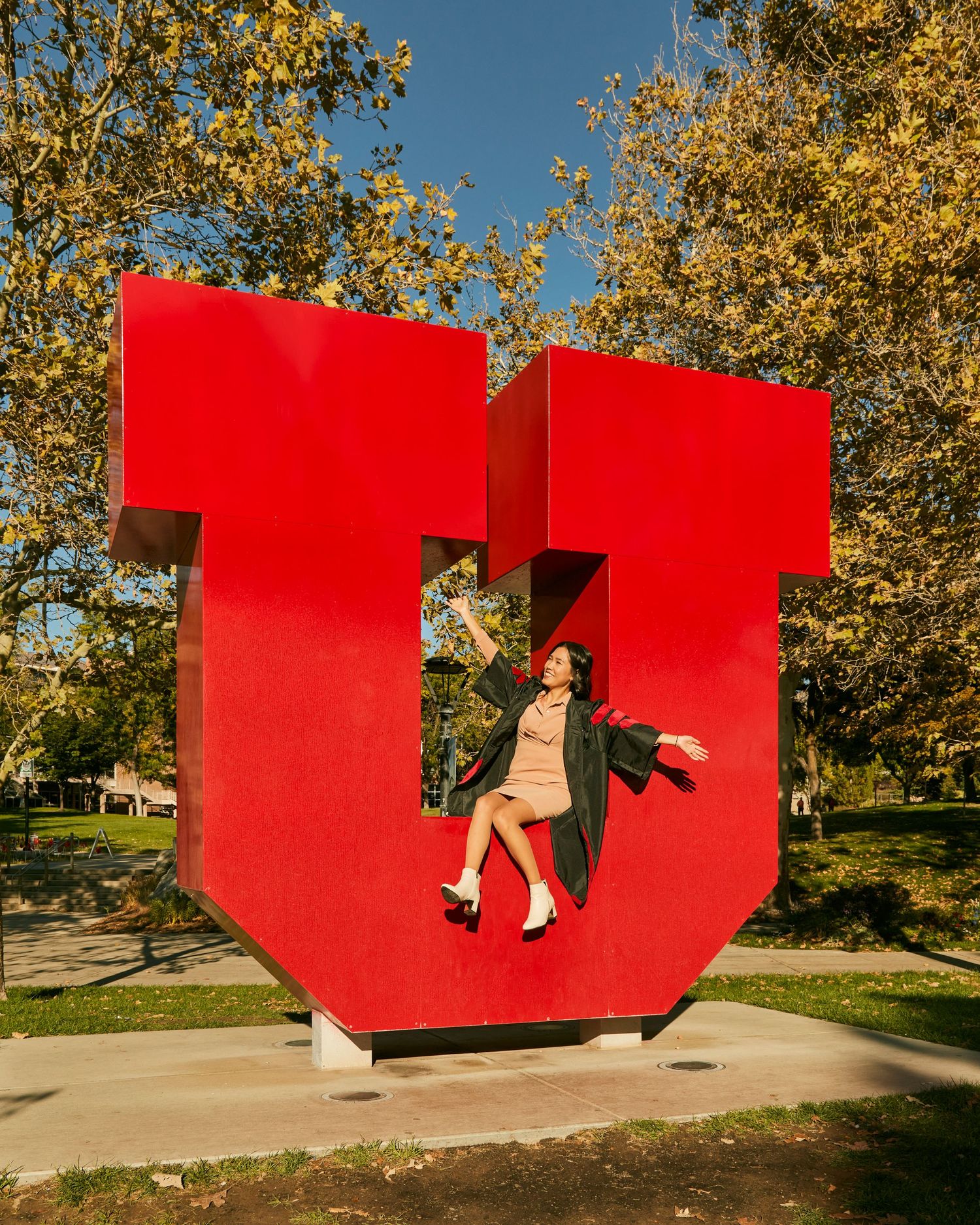 A figure poses playfully on a large red block letter U sculpture outdoors on a sunny autumn day.