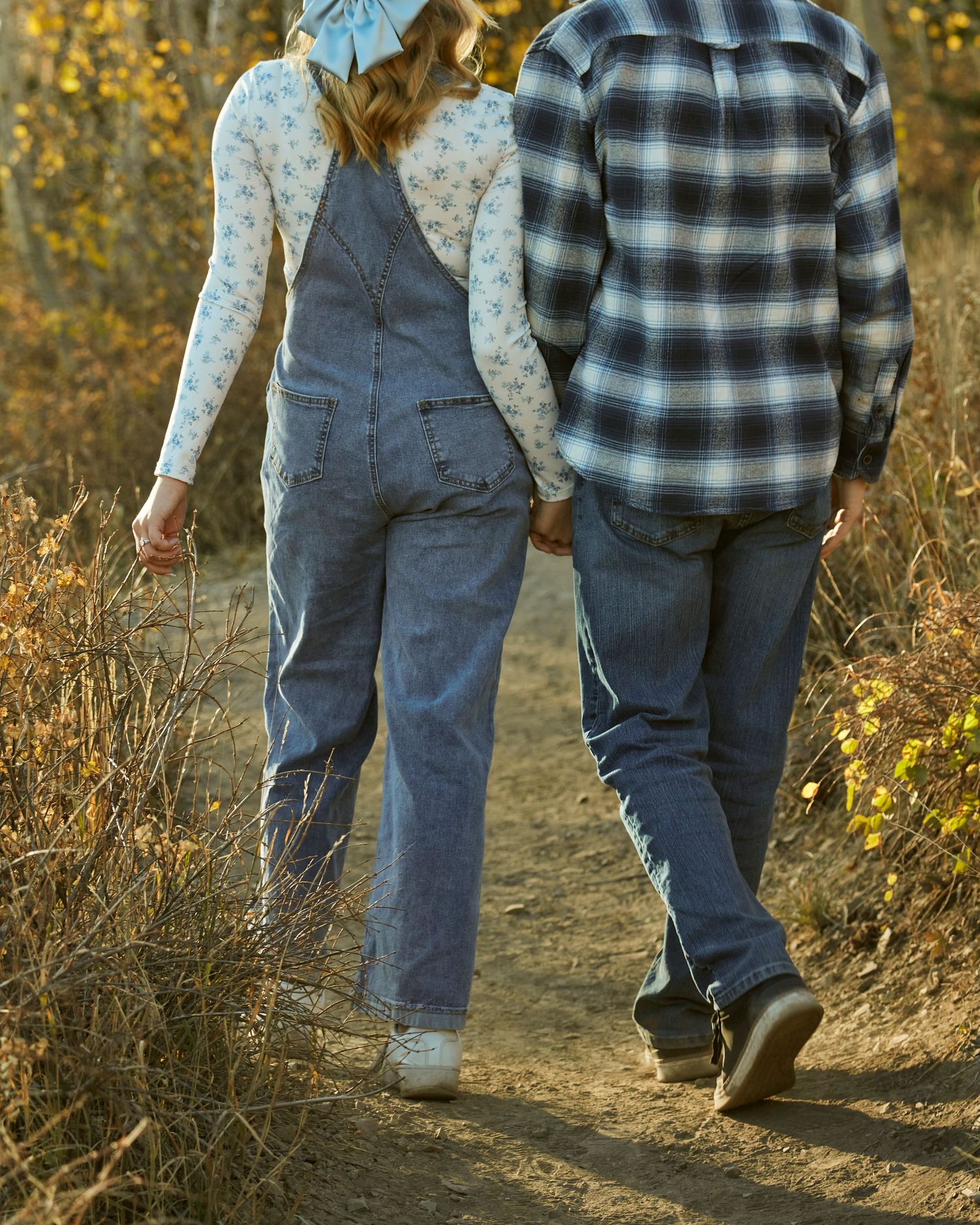Couple walking hand in hand on a trail wearing casual denim and plaid clothing.