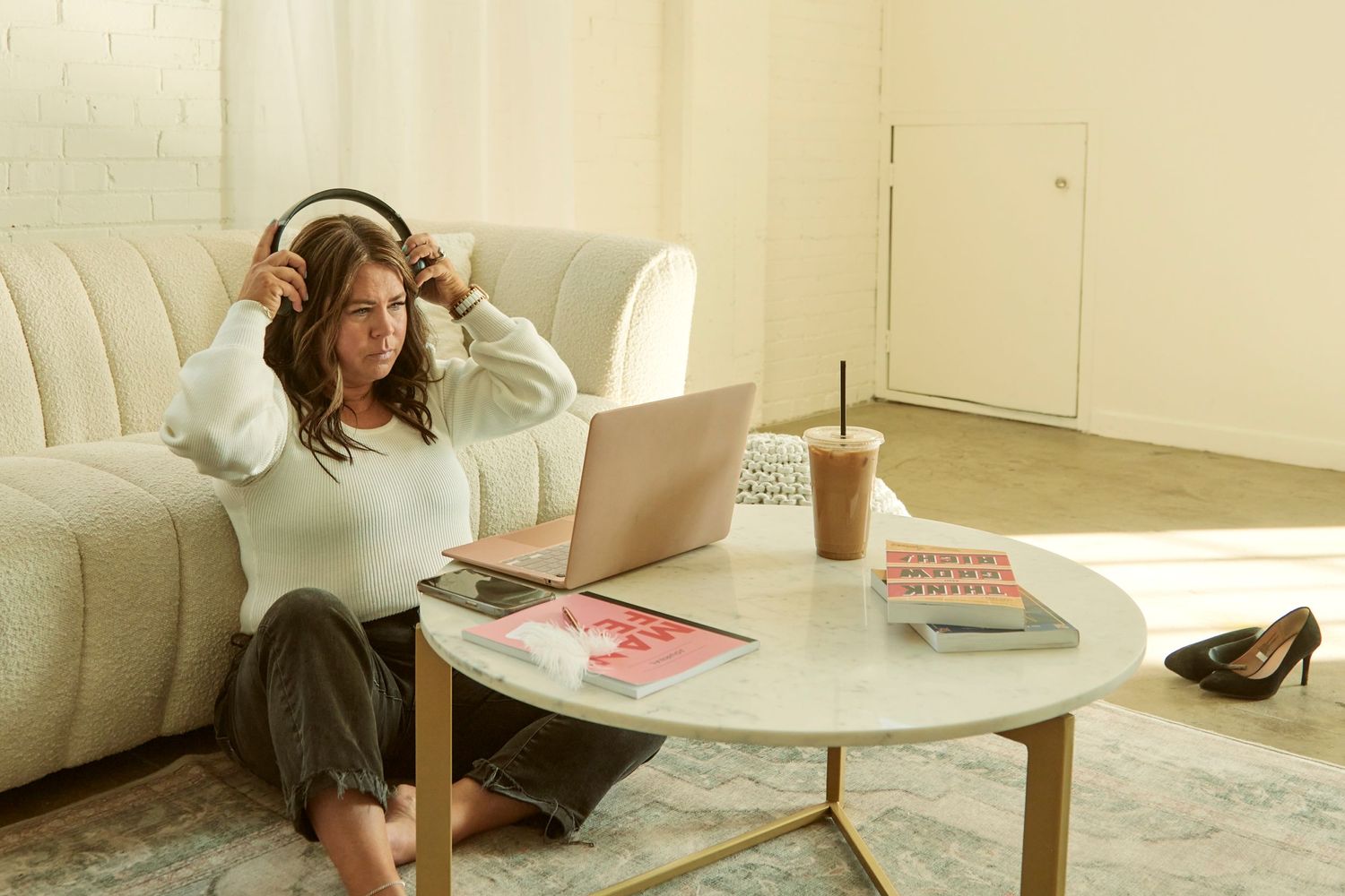 A cozy home office setup with a laptop, coffee, and accessories on a round table next to a cream-colored couch.