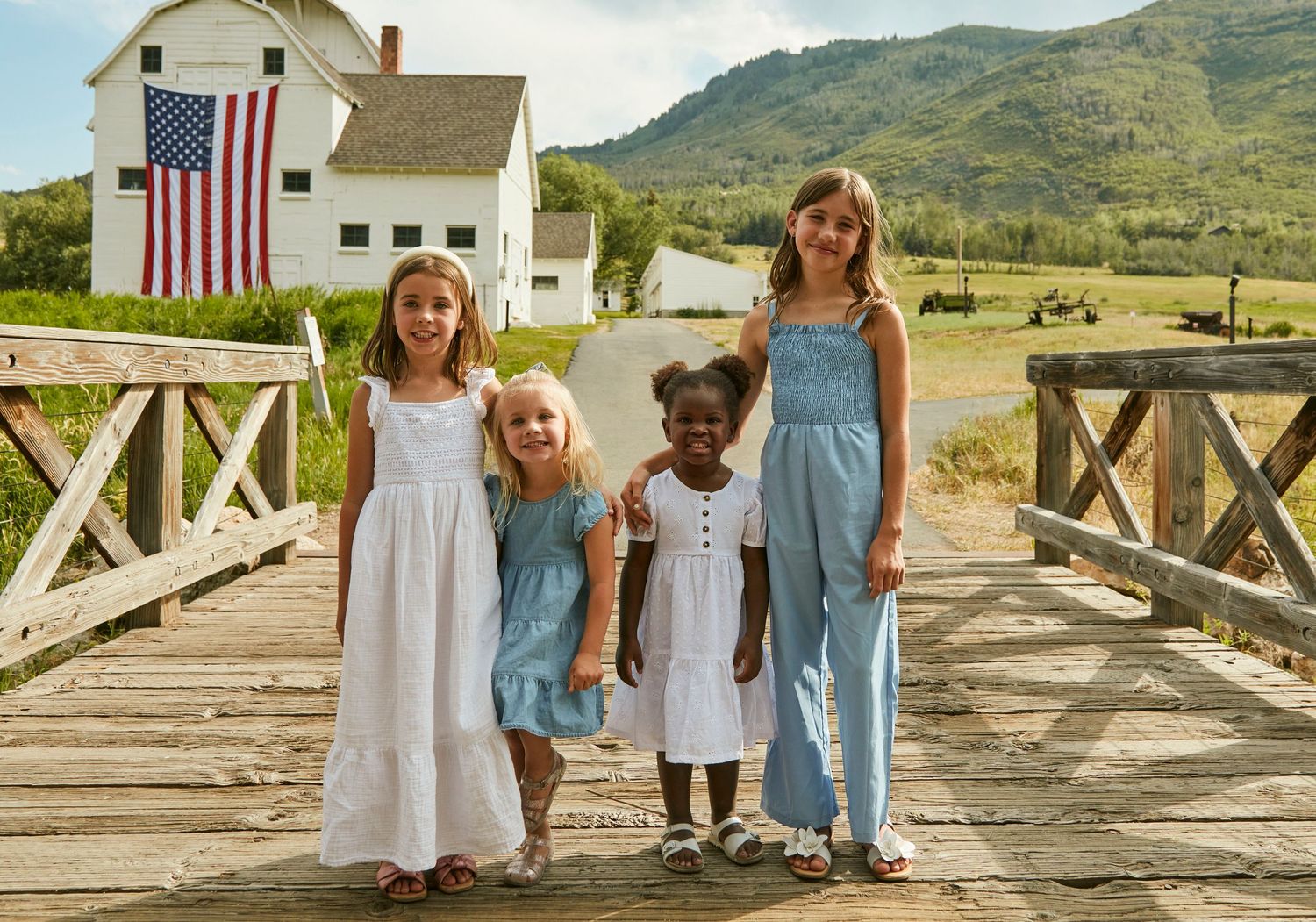 Group portrait on wooden bridge with American flag and white farmhouse in background.