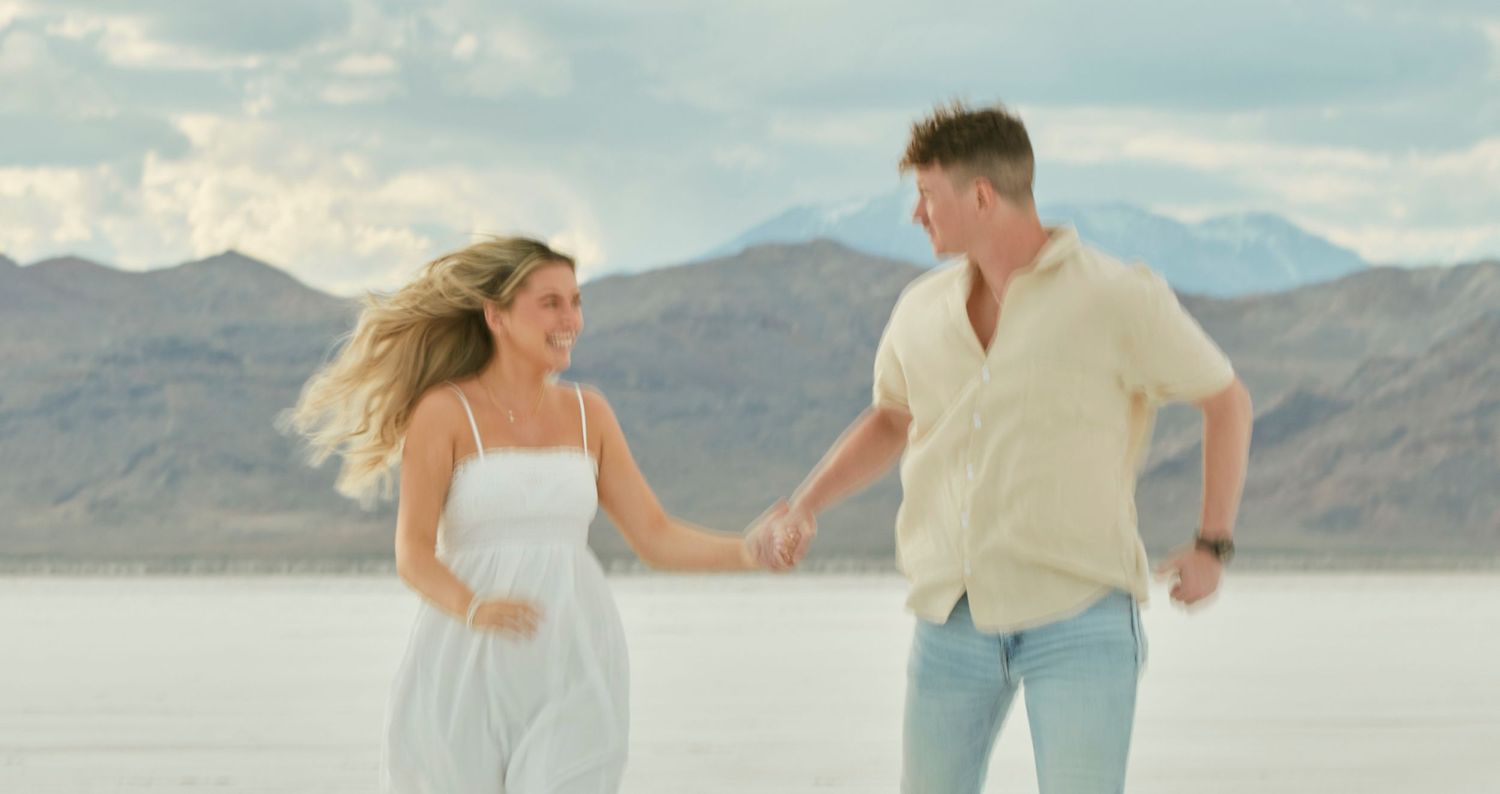 Two people running playfully on a salt flat with mountains in the distance.